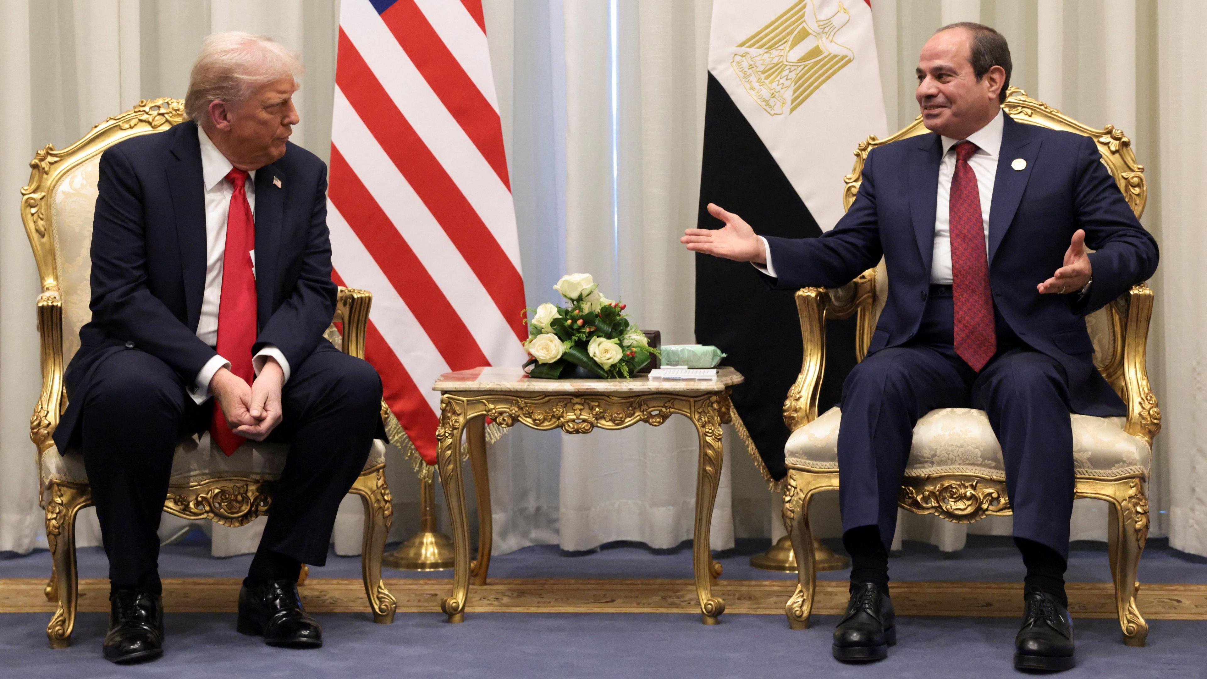 President Trump wears a dark blue suit with a red tie and white shirt sitting in a gold chair. Egypt's President Abdel Fattah al-Sisi wears a dark blue suit with a white shirt and red tie and sits in a gold chair next to him.