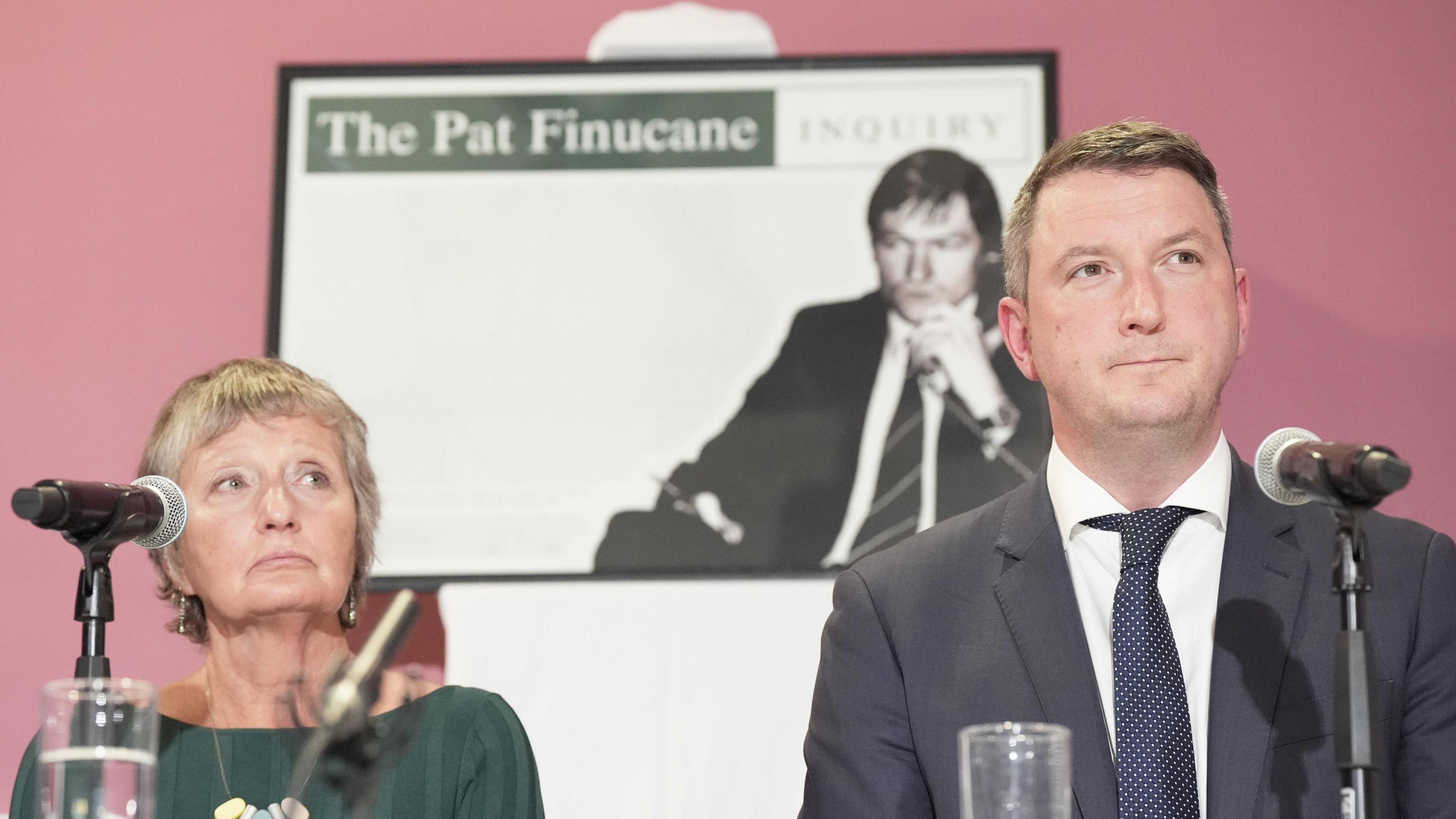 Geraldine Finucane sitting behind a microphone beside her son, MP John Finucane, at a press conference.  A TV screen showing a picture of the late Pat Finucane is behind them.