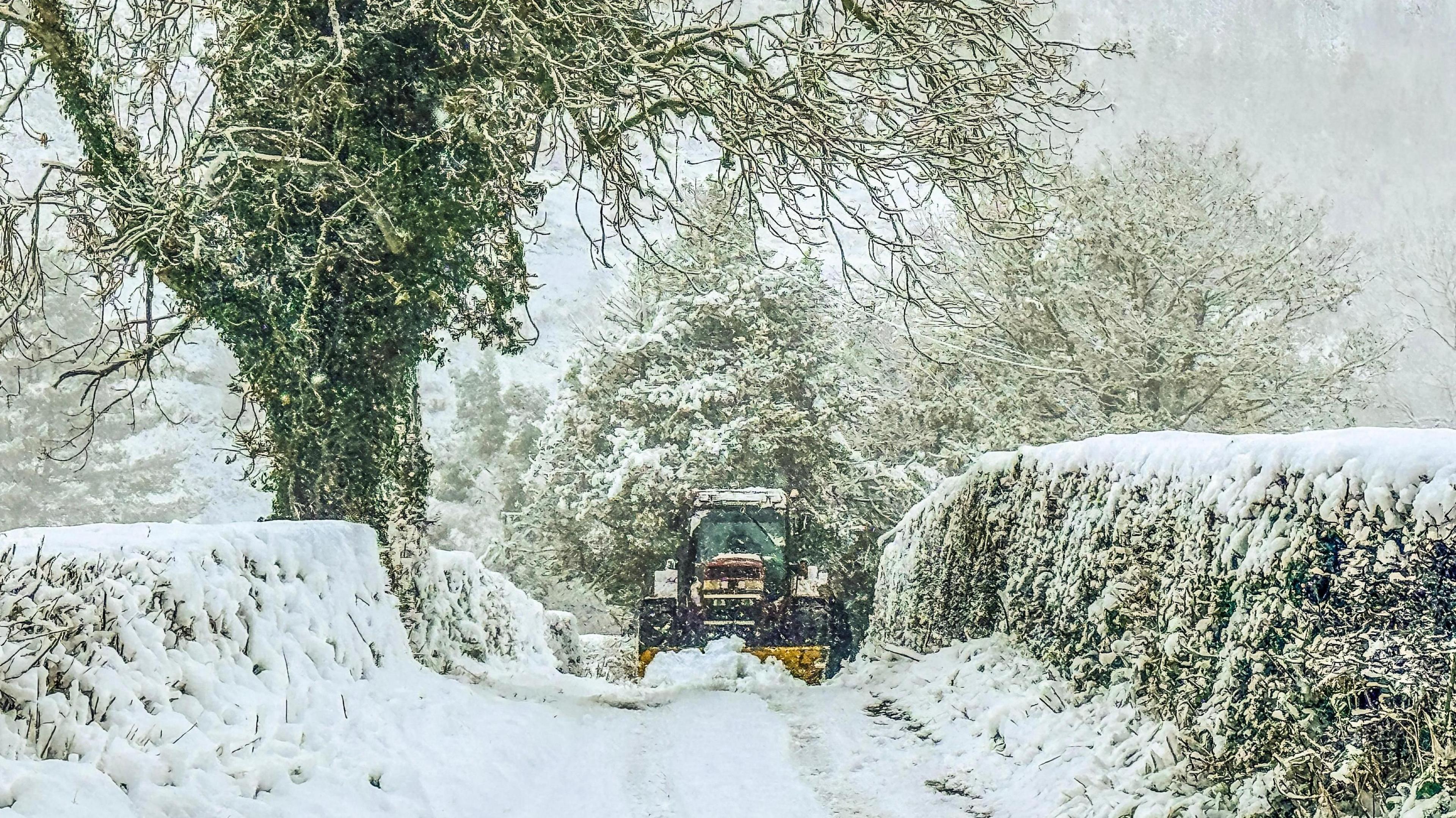 Tractor comes up a lane in Llanfair Dyffryn Clwyd in Denbighshire, surrounded by white snow. 