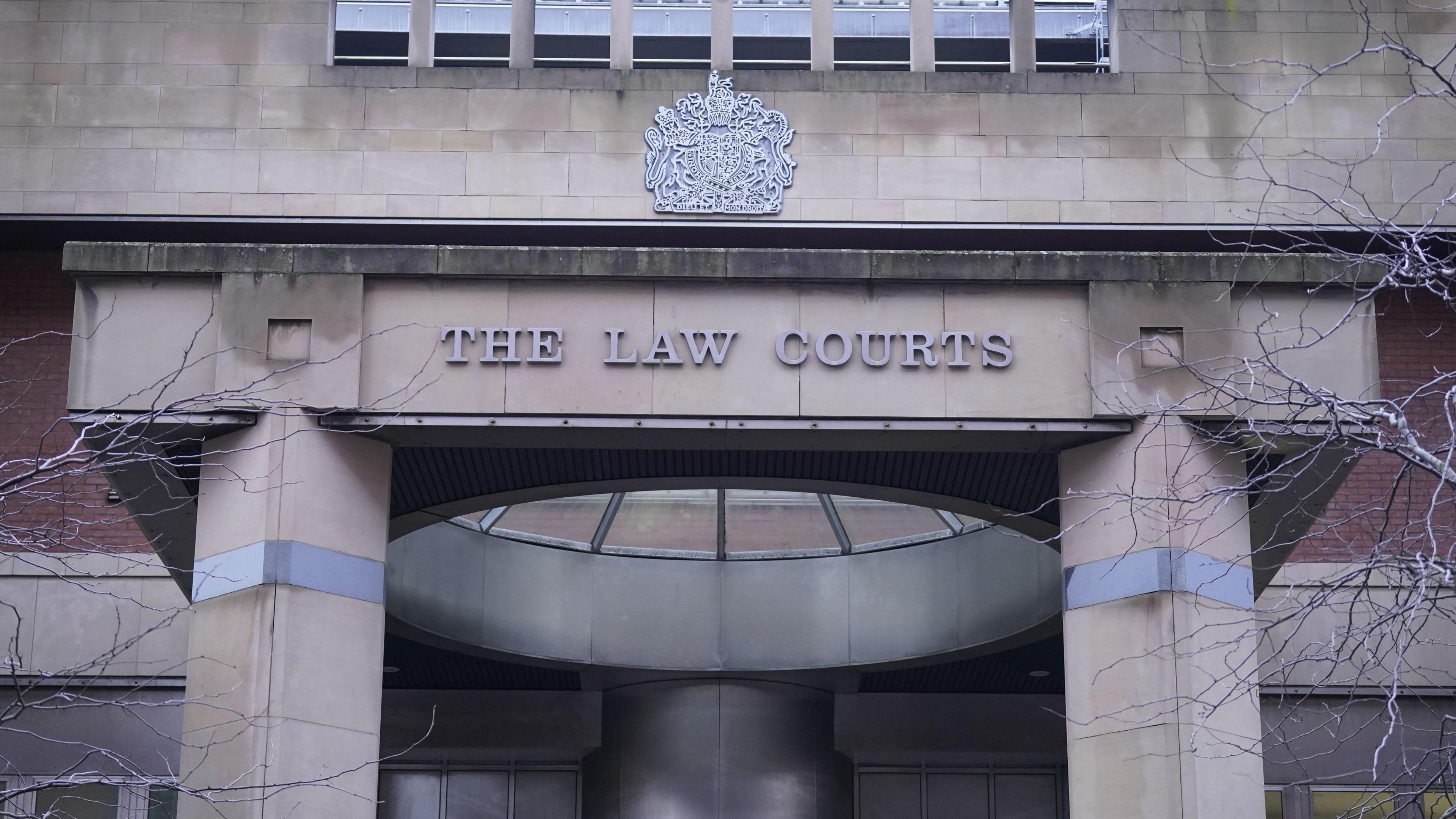 The stone front of a large building, with two columns and a glass dome. A sign reads The Law Courts and there is a Royal Coat of Arms​​ above the sign.