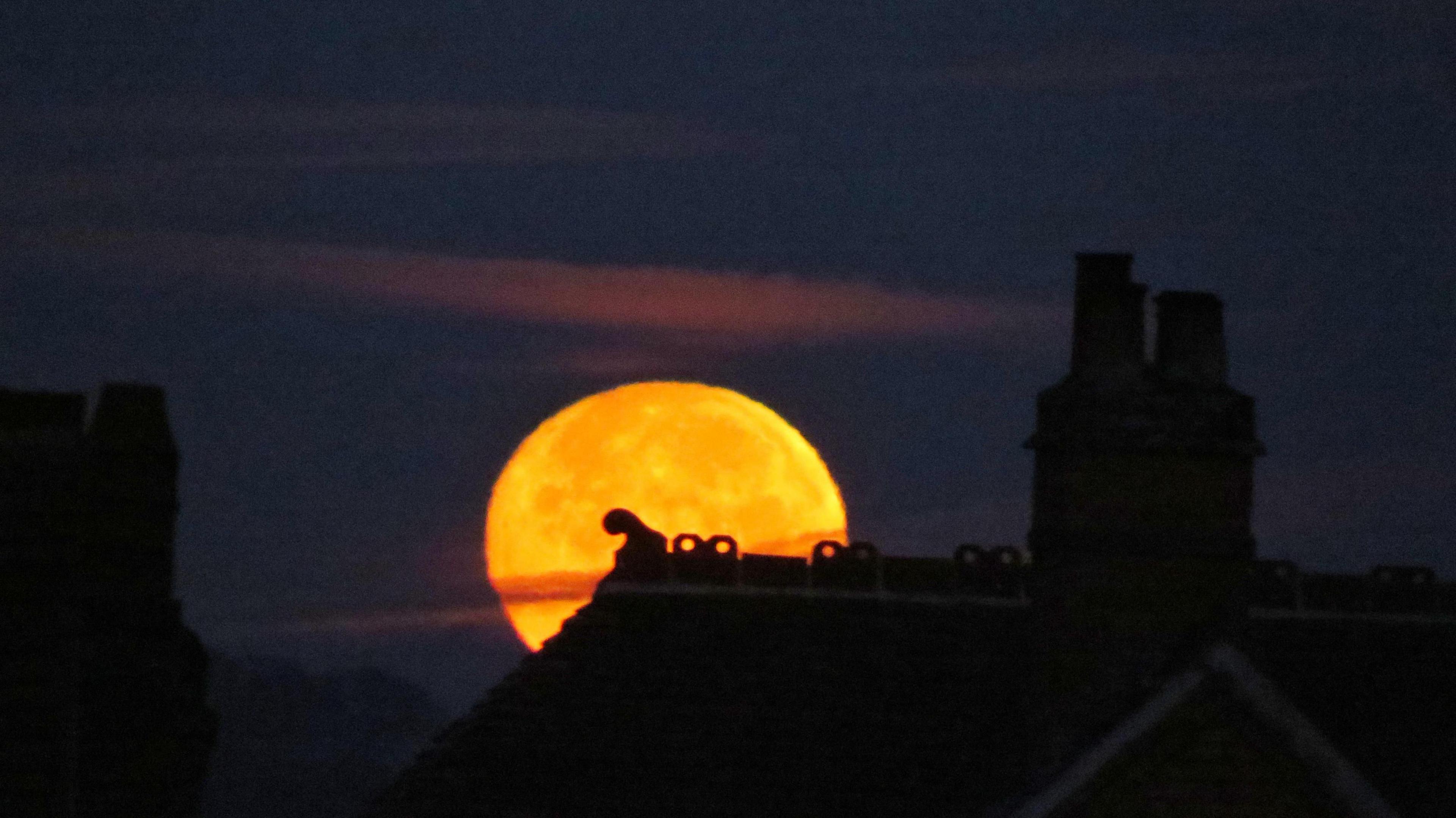 An orange-coloured supermoon behind a roof and a chimney stack