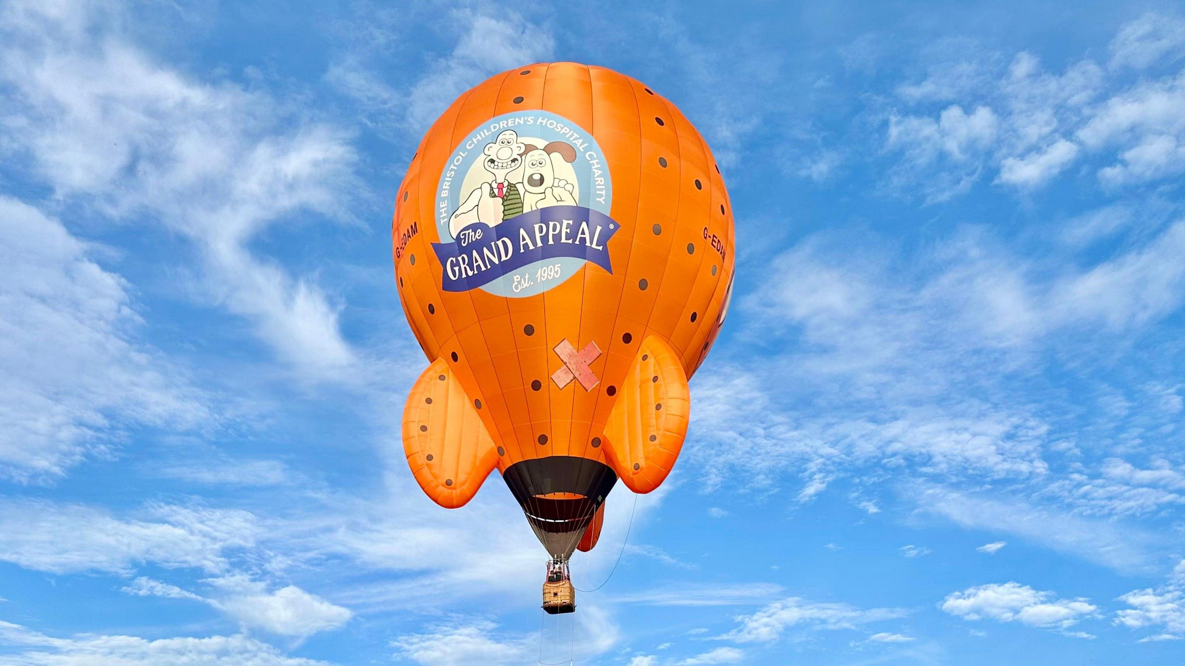 An orange hot air balloon in the shape of Wallace and Gromit's Rocket. The balloon has The Wallace & Gromit Grand Appeal logo printed on the front.