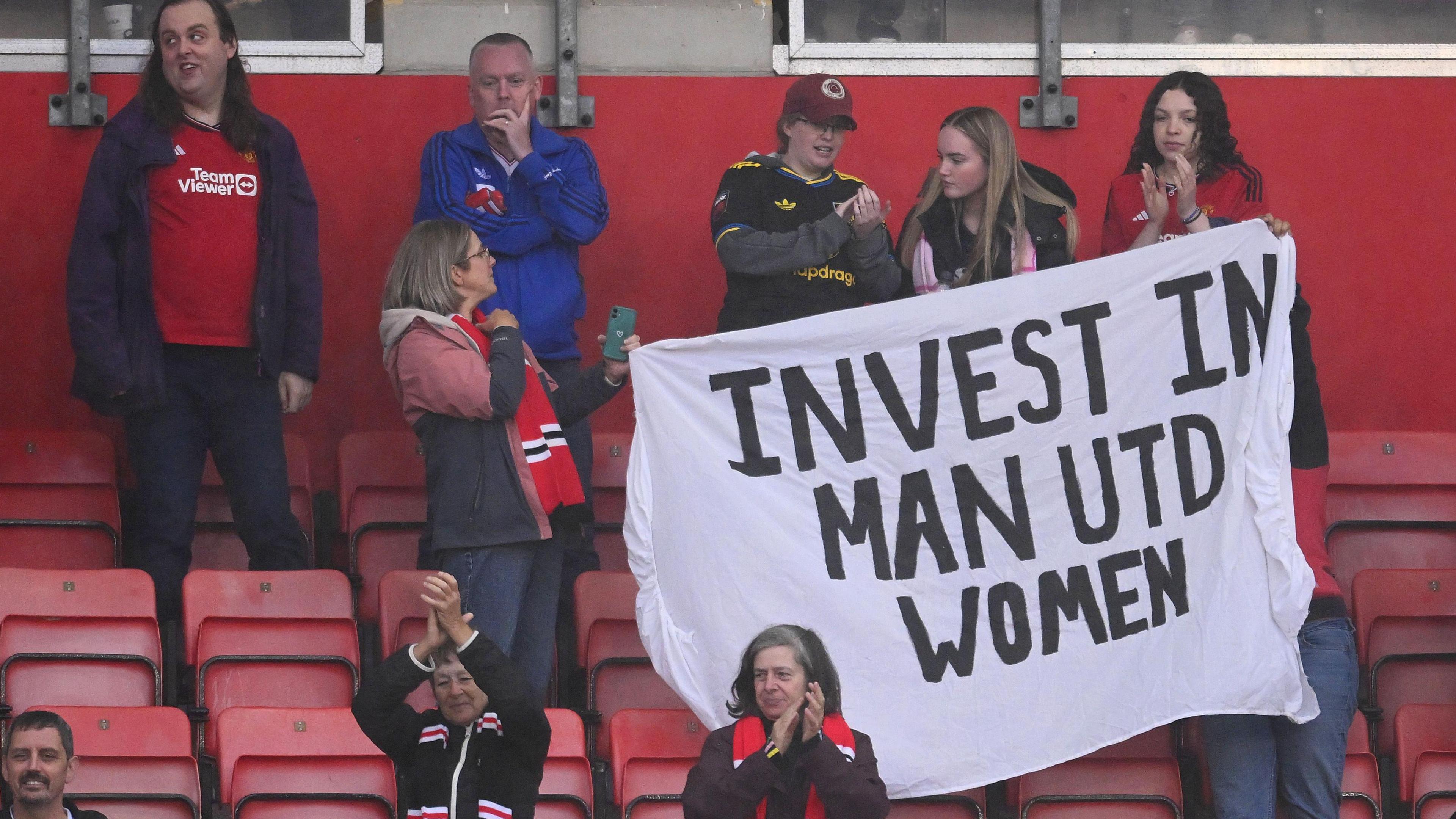 Fans hold up a banner saying 'invest in Man Utd women' during a WSL match in September