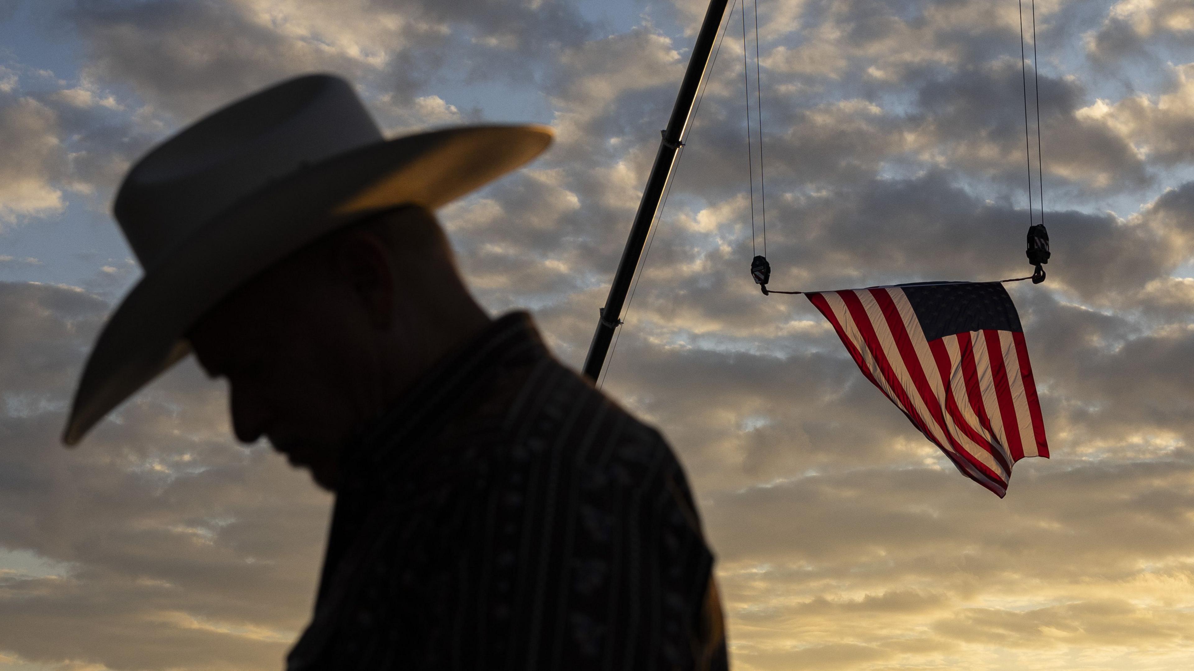 Image shows a silhouette of a man walking past an American flag