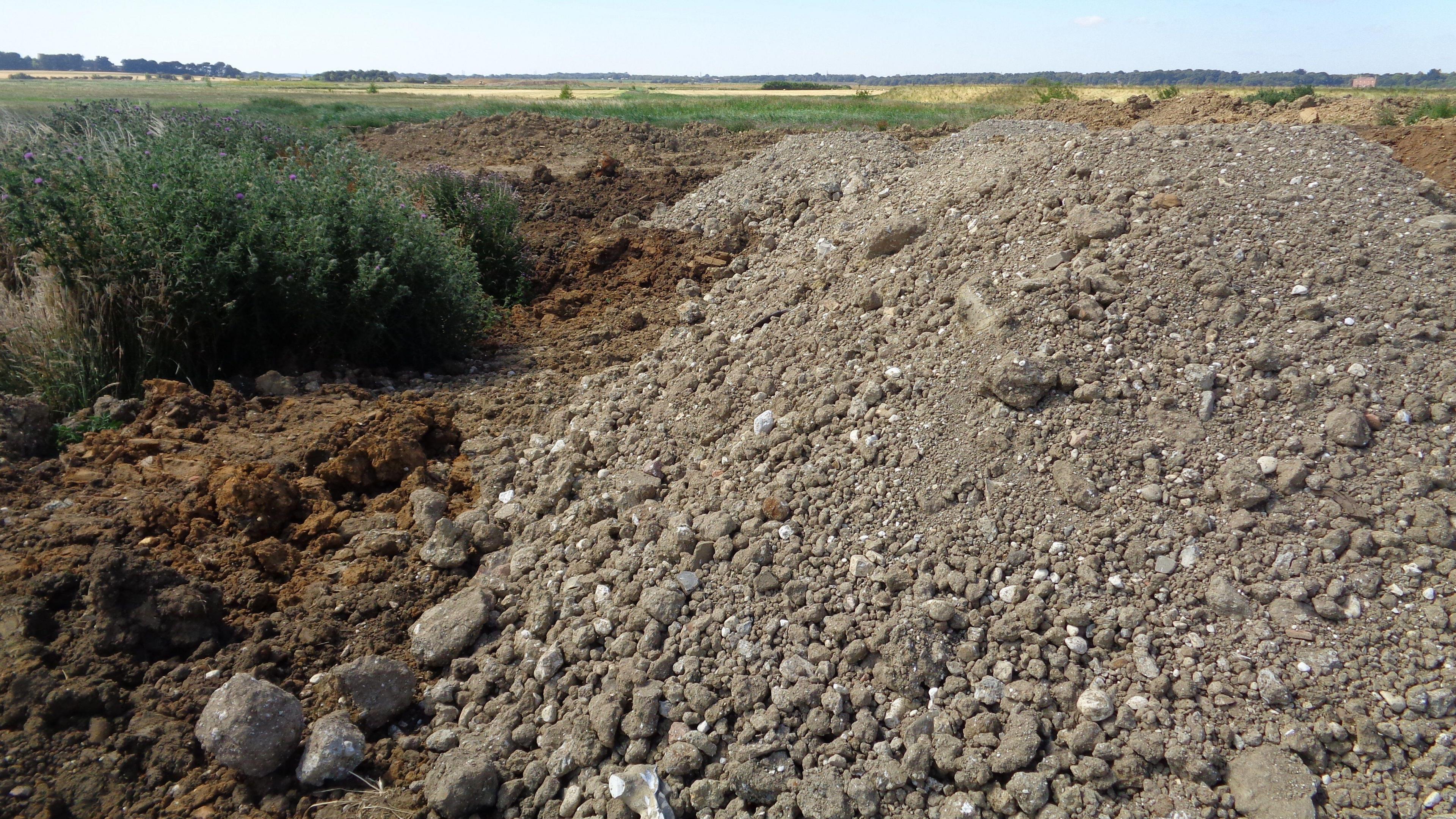 Mounds of rocks and dirt in the foreground with foliage and fields in the background.