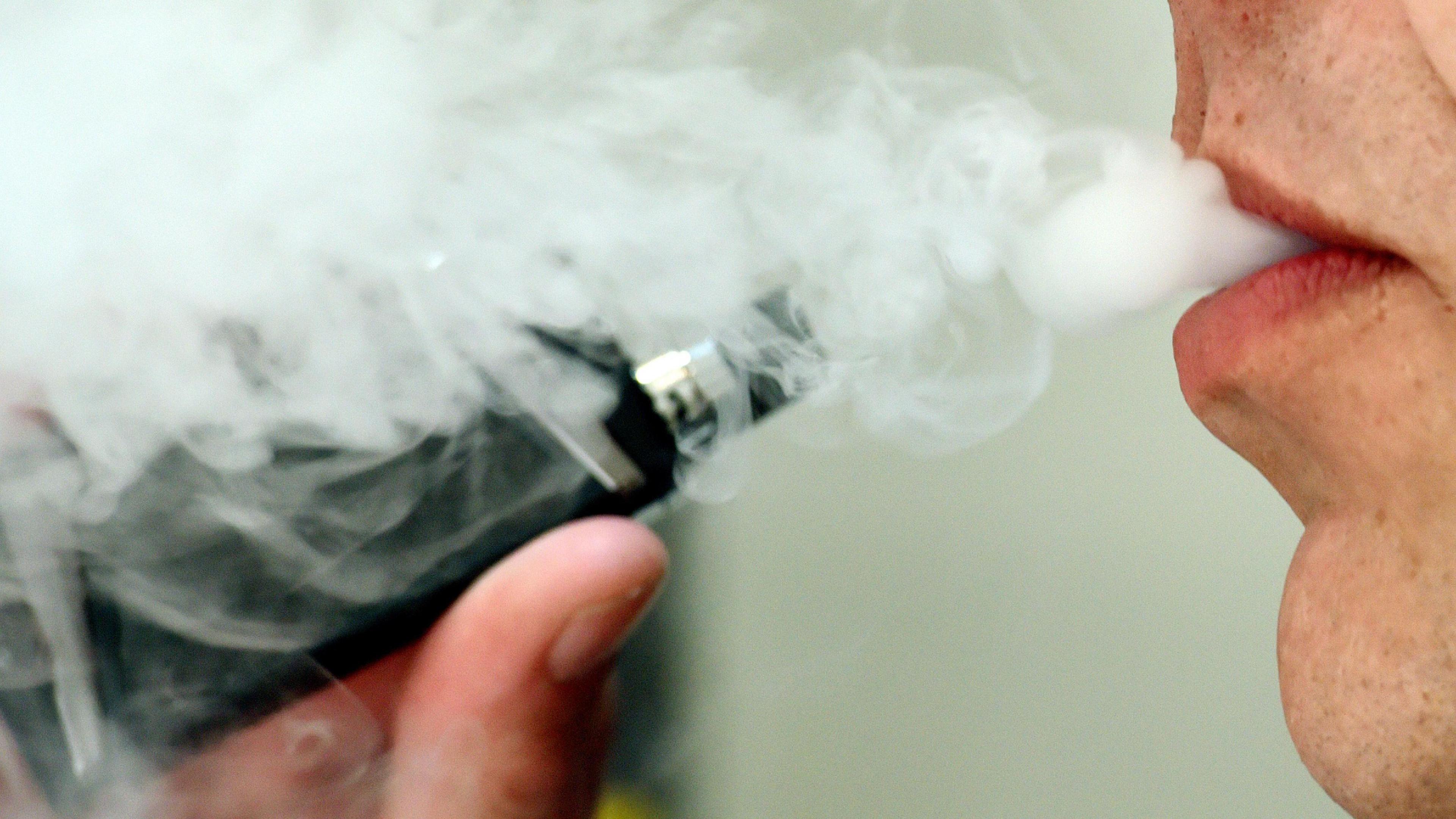 A face blowing smoke out of its mouth. A vape pen is being taken away from the mouth.