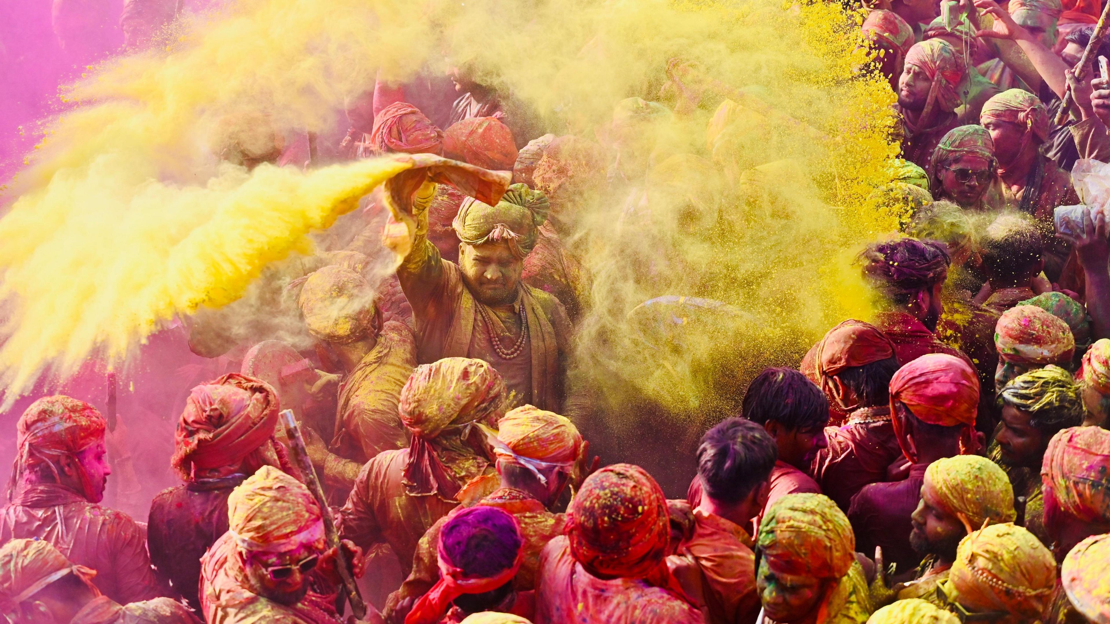 A colour-smeared group of people celebrating Holi, seen throwing yellow powder on themselves as part of the festival