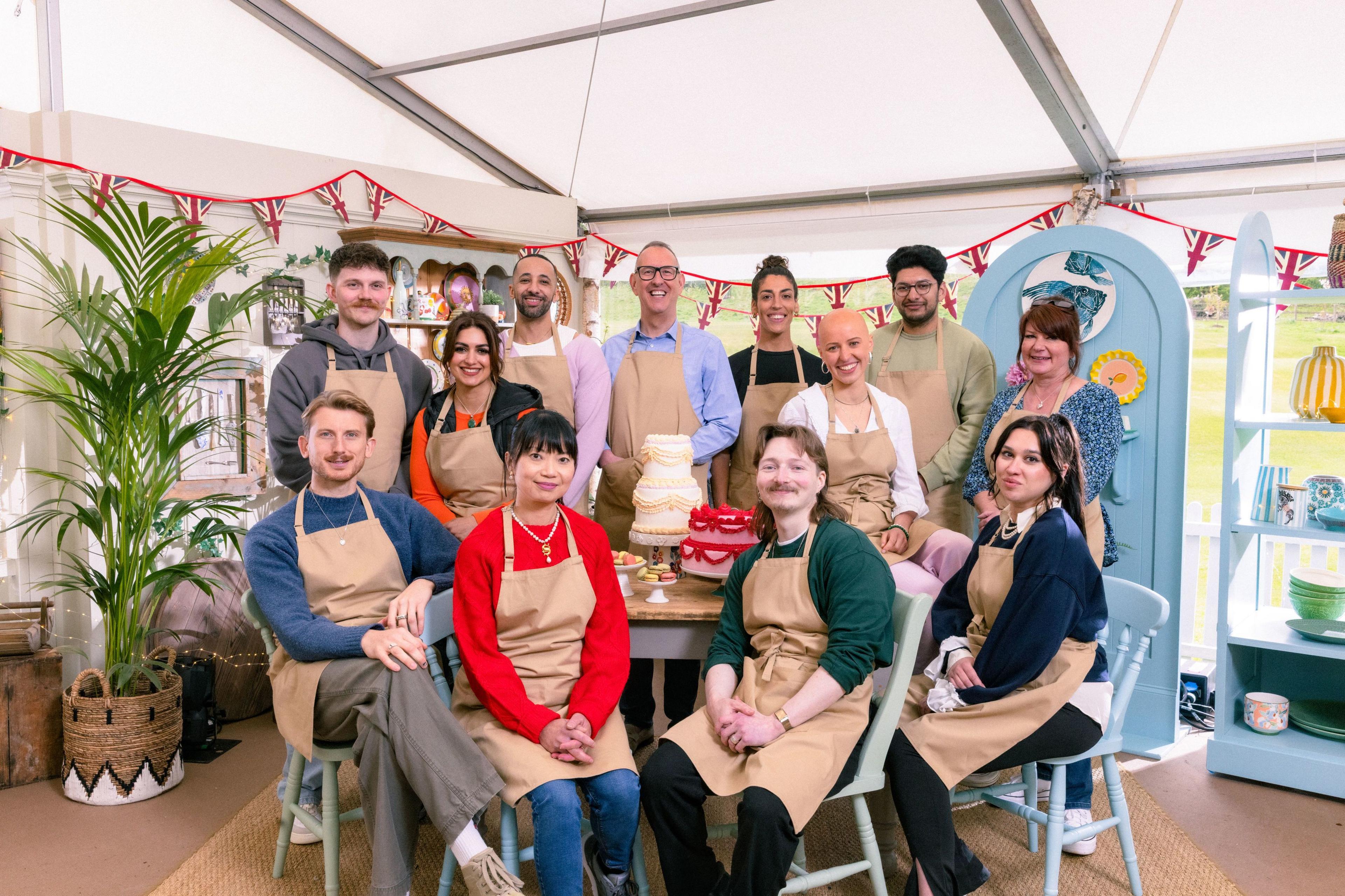 The Great British Bake Off Series 16 contestants (back row, left to right) Toby, Nadia, Aaron, Leighton, Jessika, Jasmine, Hassan and Lesley; and (front row, left to right) Tom, Pui Man, Iain and Nataliia. It shows the group of people, some stood and other sat with aprons on in a tent.