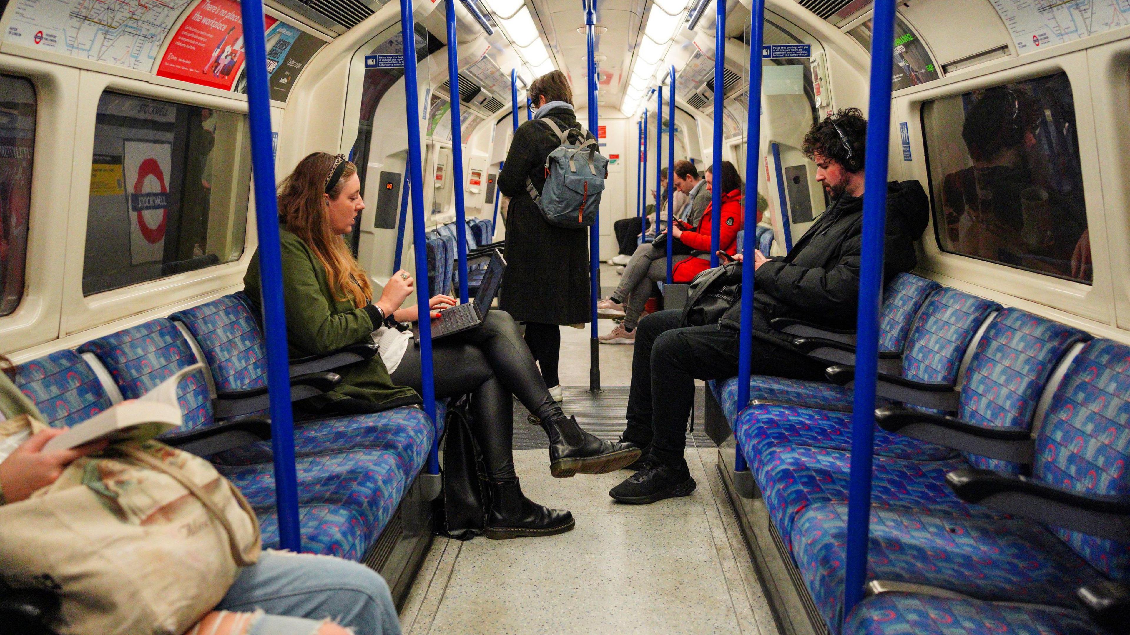 Inside a Tube carriage, passengers are sitting on seats