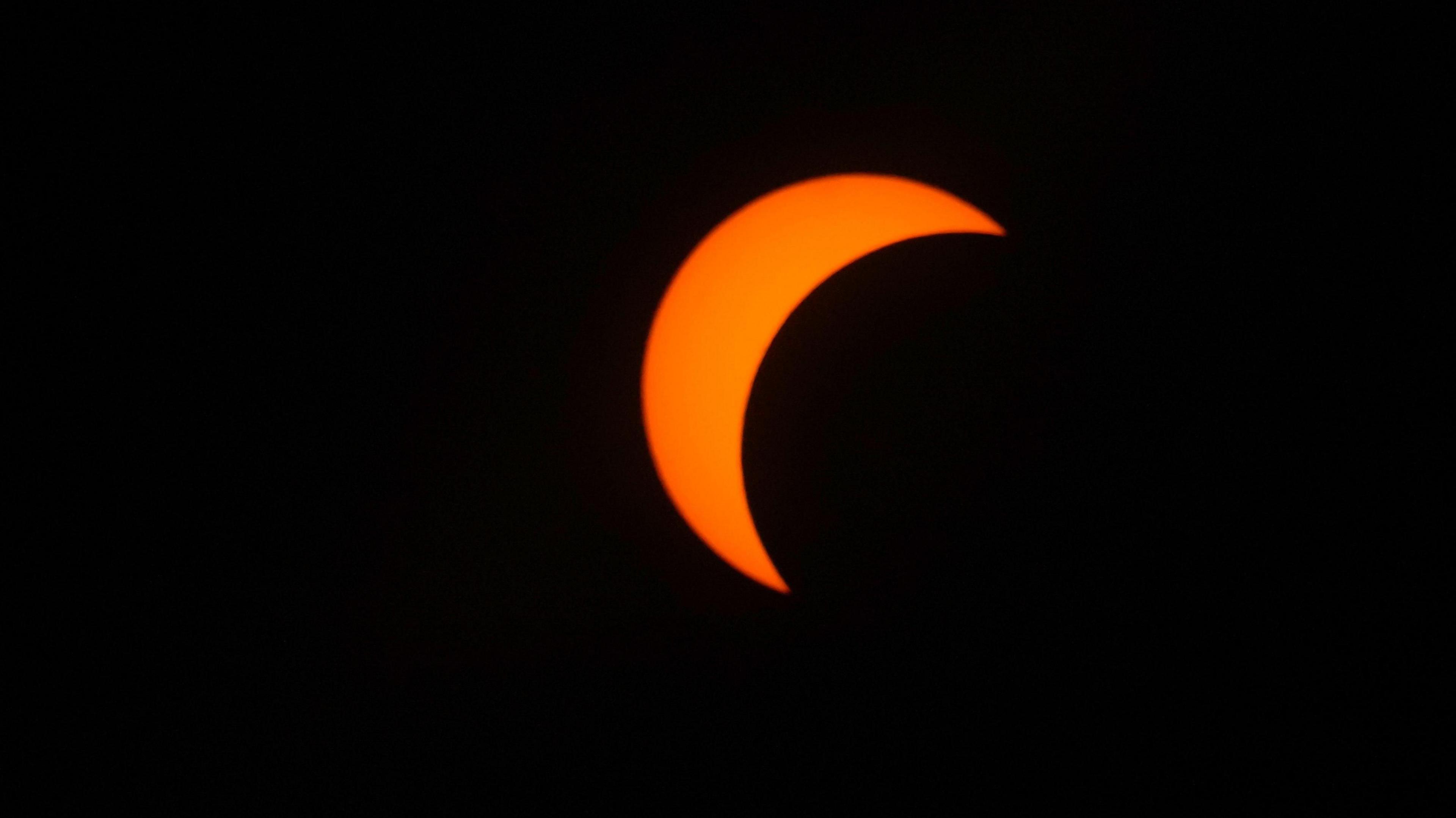 Black Moon passes right to left in front of an orange Sun