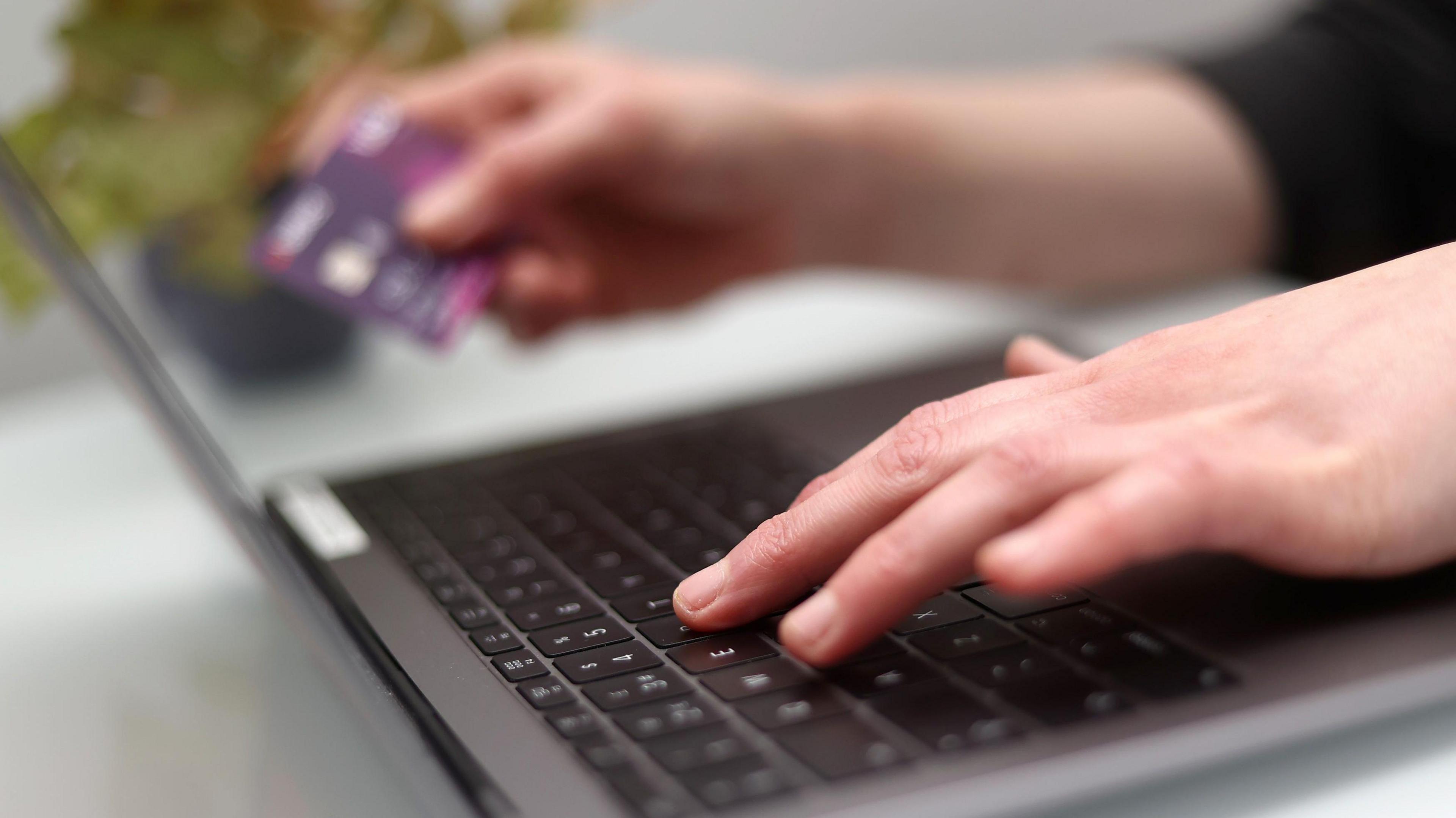 A woman uses a laptop as she holds a bank card. 