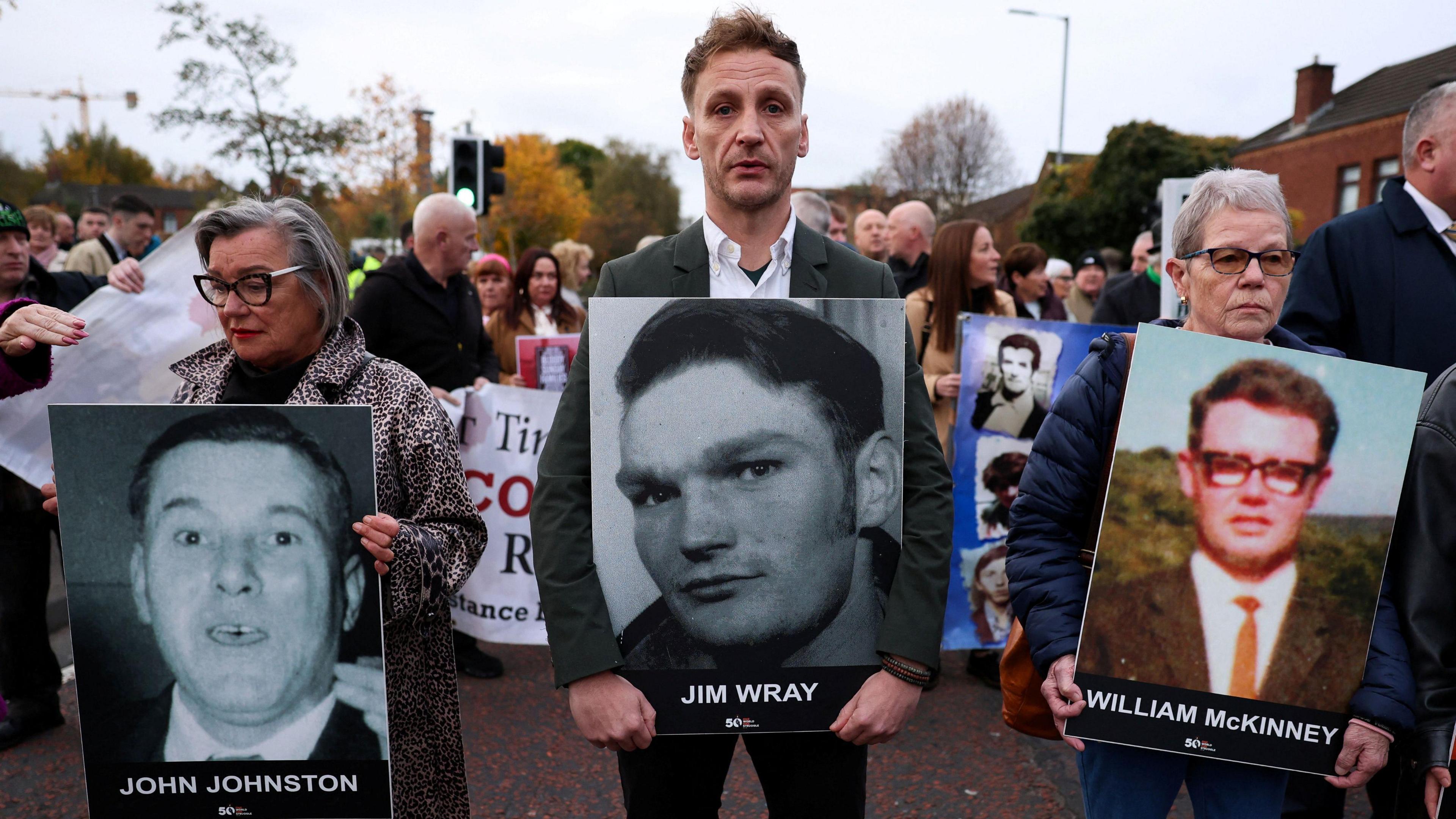 A crowd gathers in the street holding placards with family members