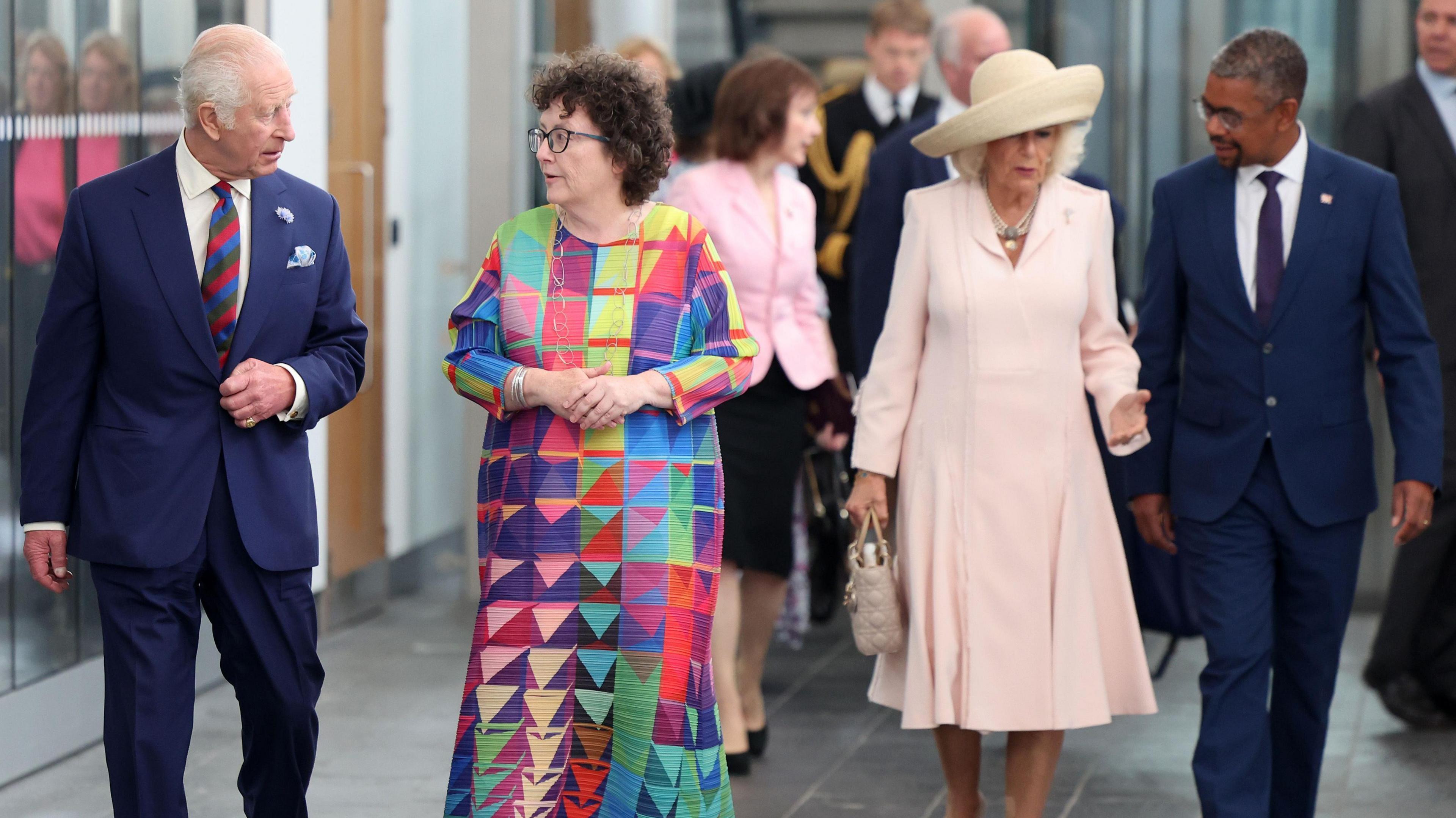 King Charles walking in the senedd foyer chatting with Elin Jones presiding officer, with Queen Camilla and First Minister Vaughan Gething walking behind them 