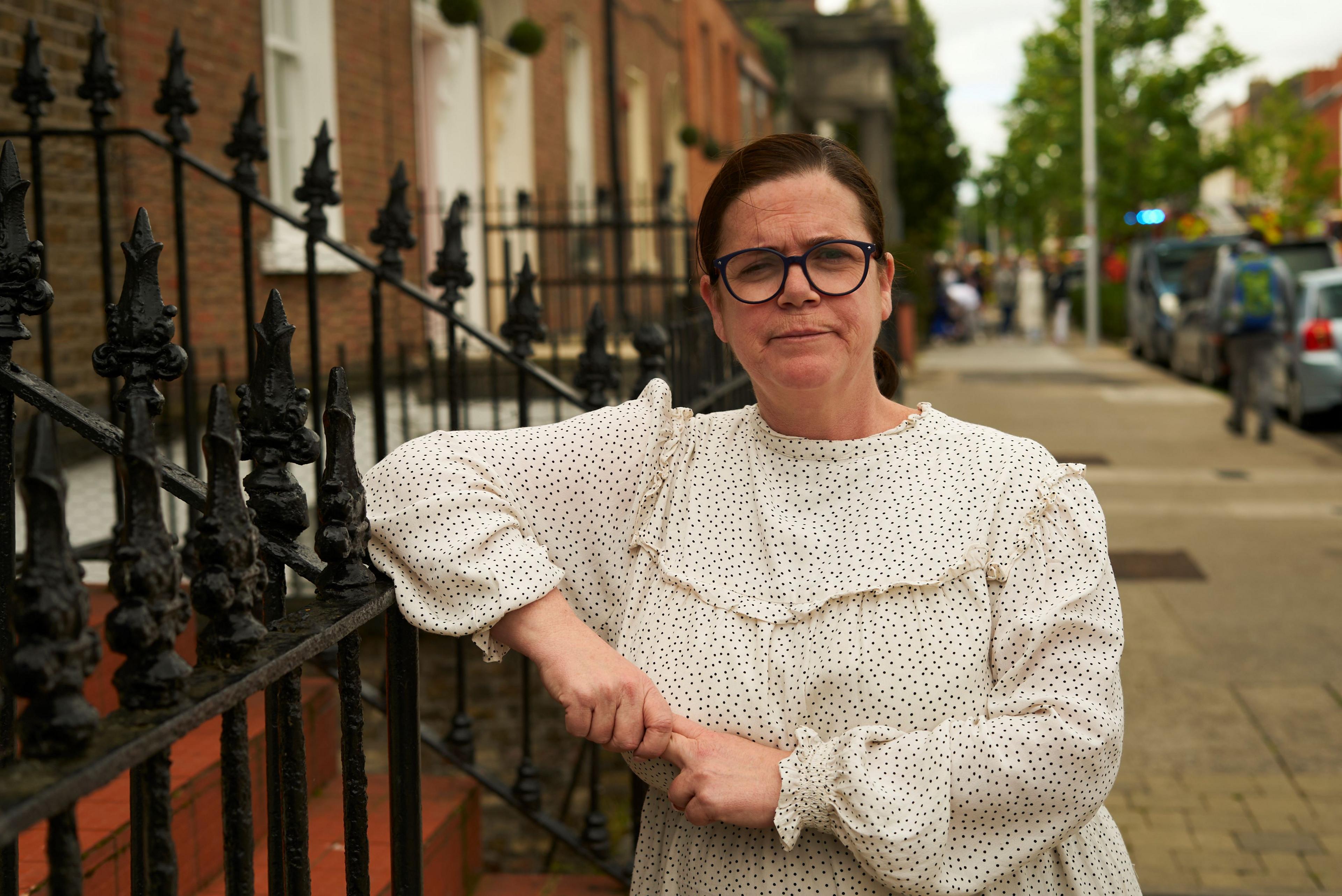 Belinda Nugent standing outside on the streets of Dublin leaning against a black metal fence