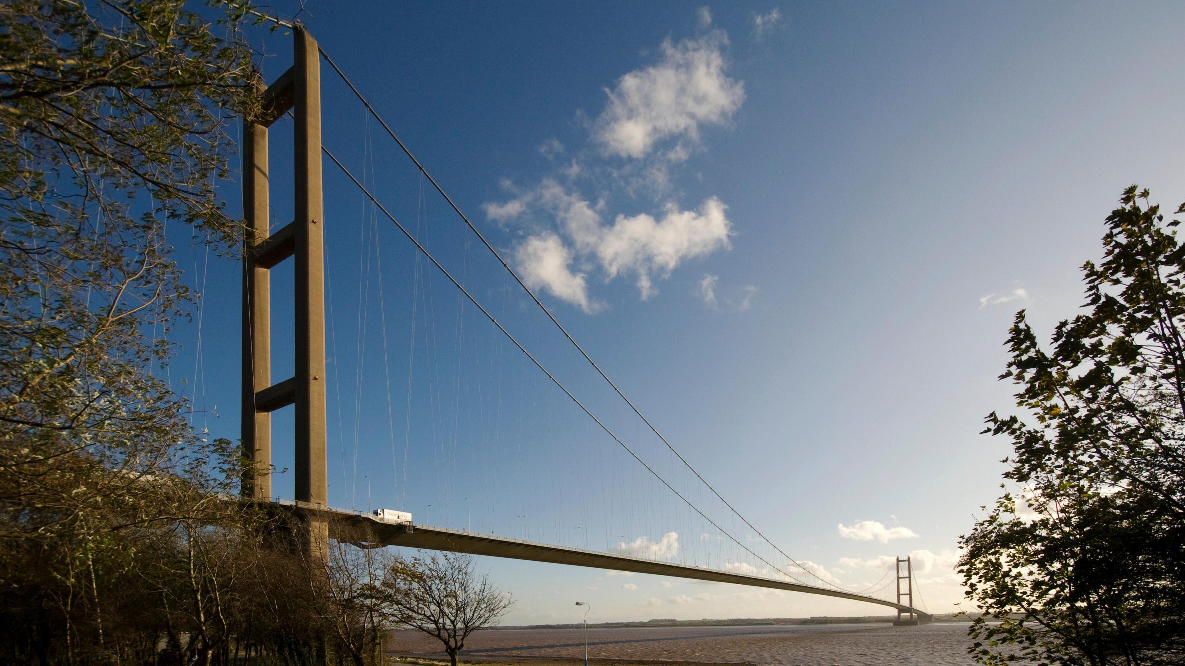 A stock image of the Humber Bridge, a large suspension bridge over the Humber Estuary on a sunny day.