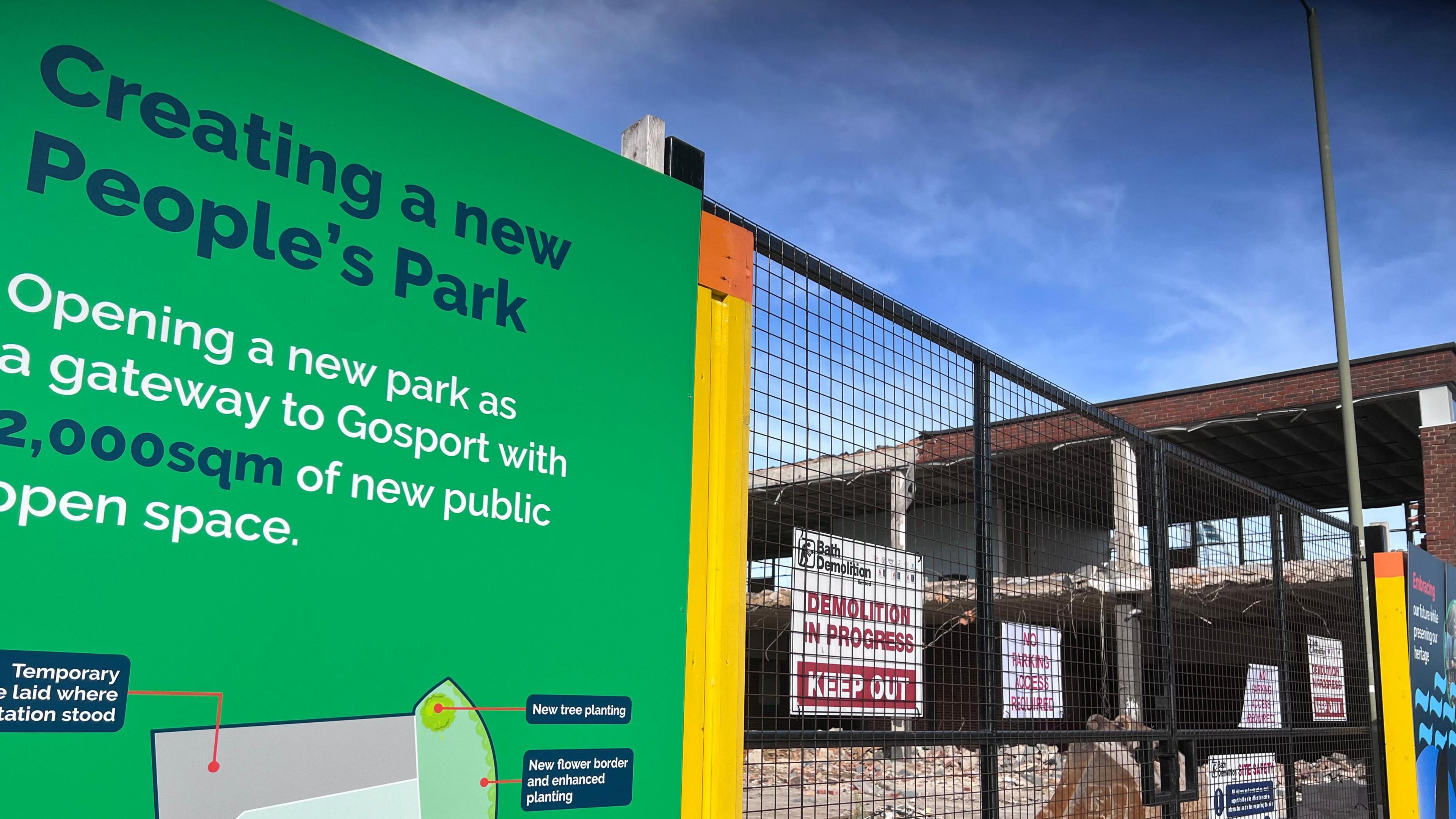 Picture shows the hoardings with the map showing the new open space design including flower borders and tree planting areas and then the fences protecting the demolition site with the words "Demolition in Progress, Keep out"
