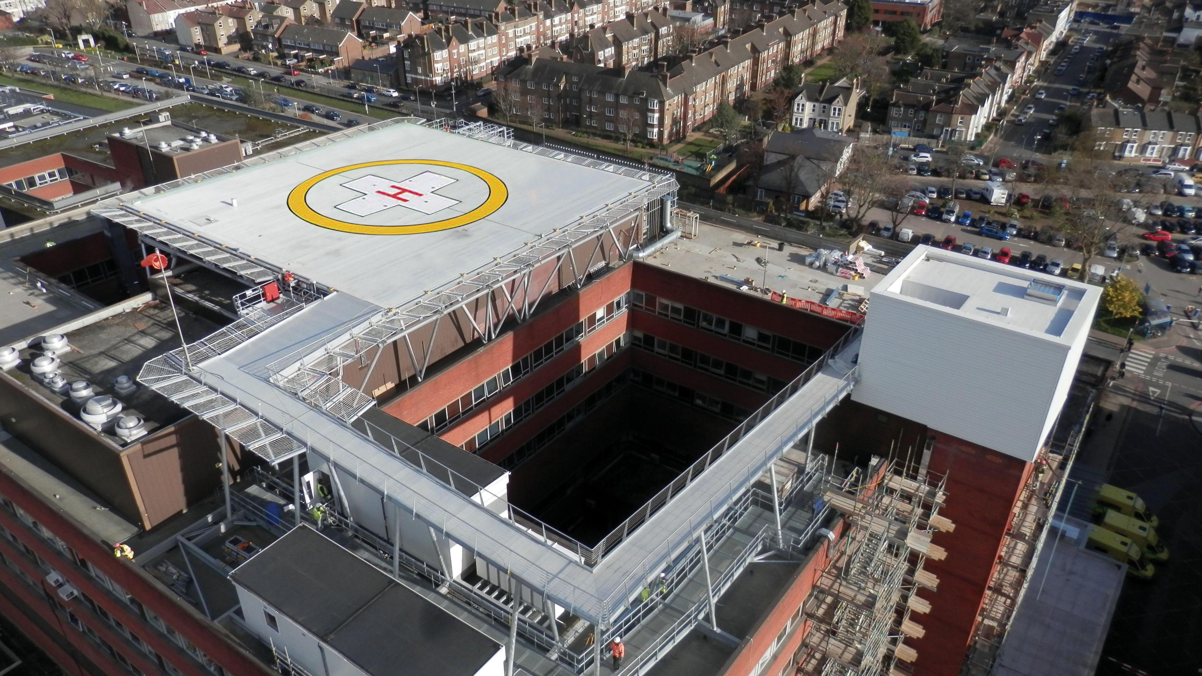 A helipad marked by a yellow circle with a white cross and the letter "H" in red in the middle. The helipad in on top of a red building.