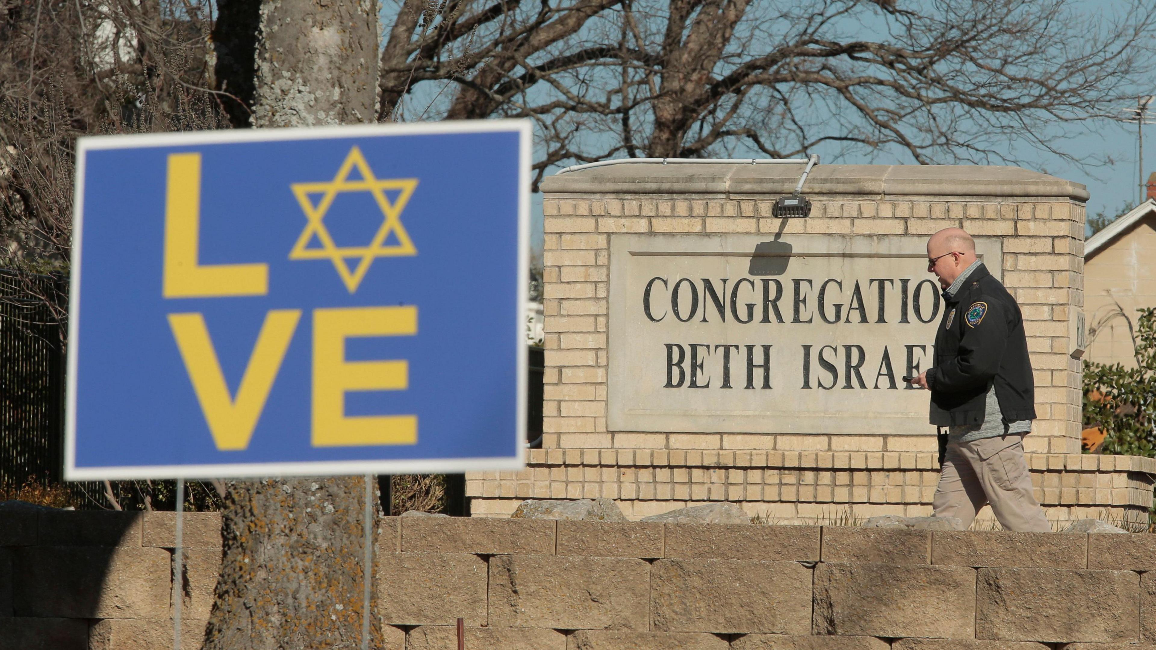 A policeman walks past the synagogue sign with a placard proclaiming the word Love with the star of David