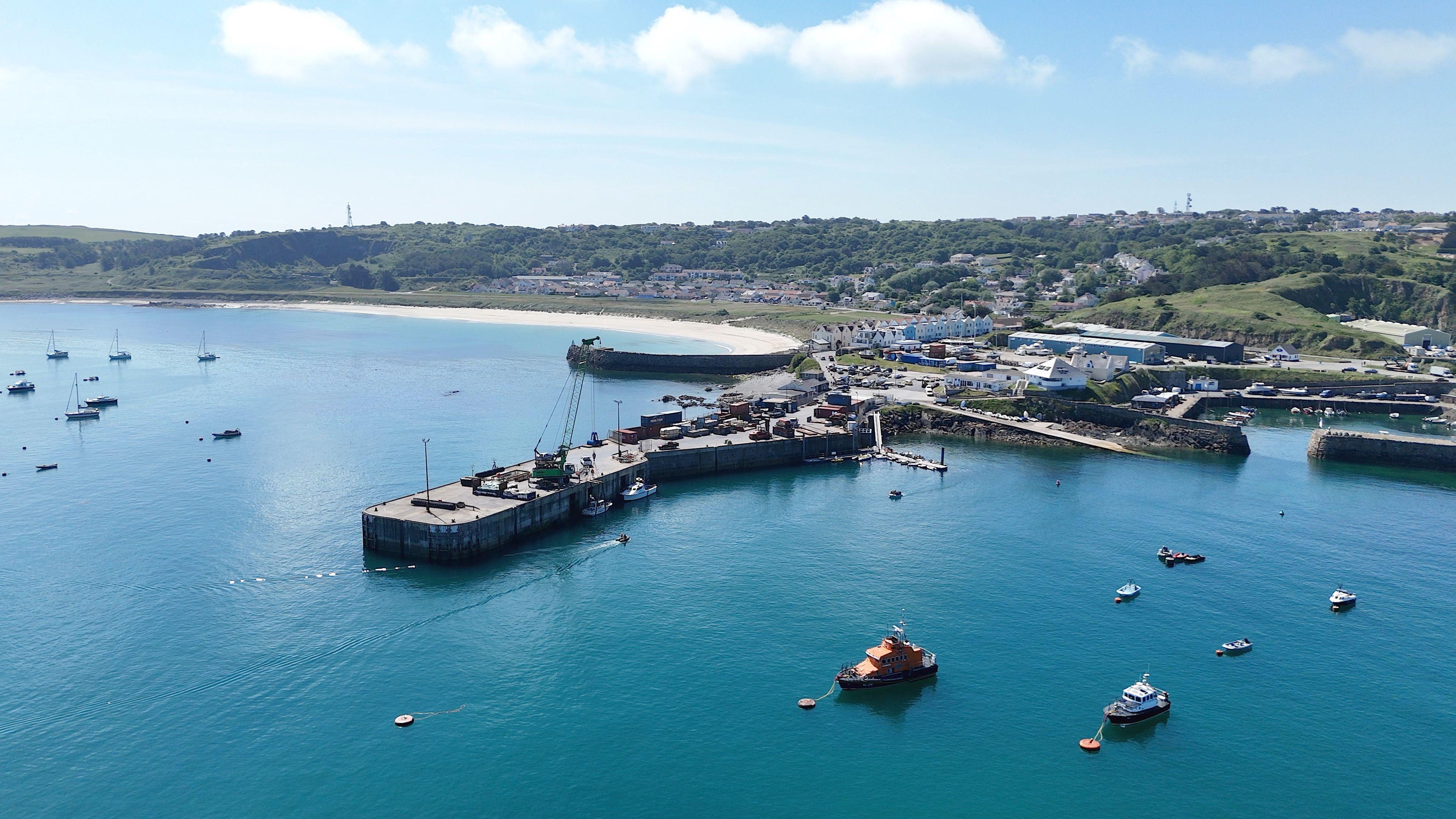 An aerial view of Alderney Harbour. The water is blue and there are boats on the water.