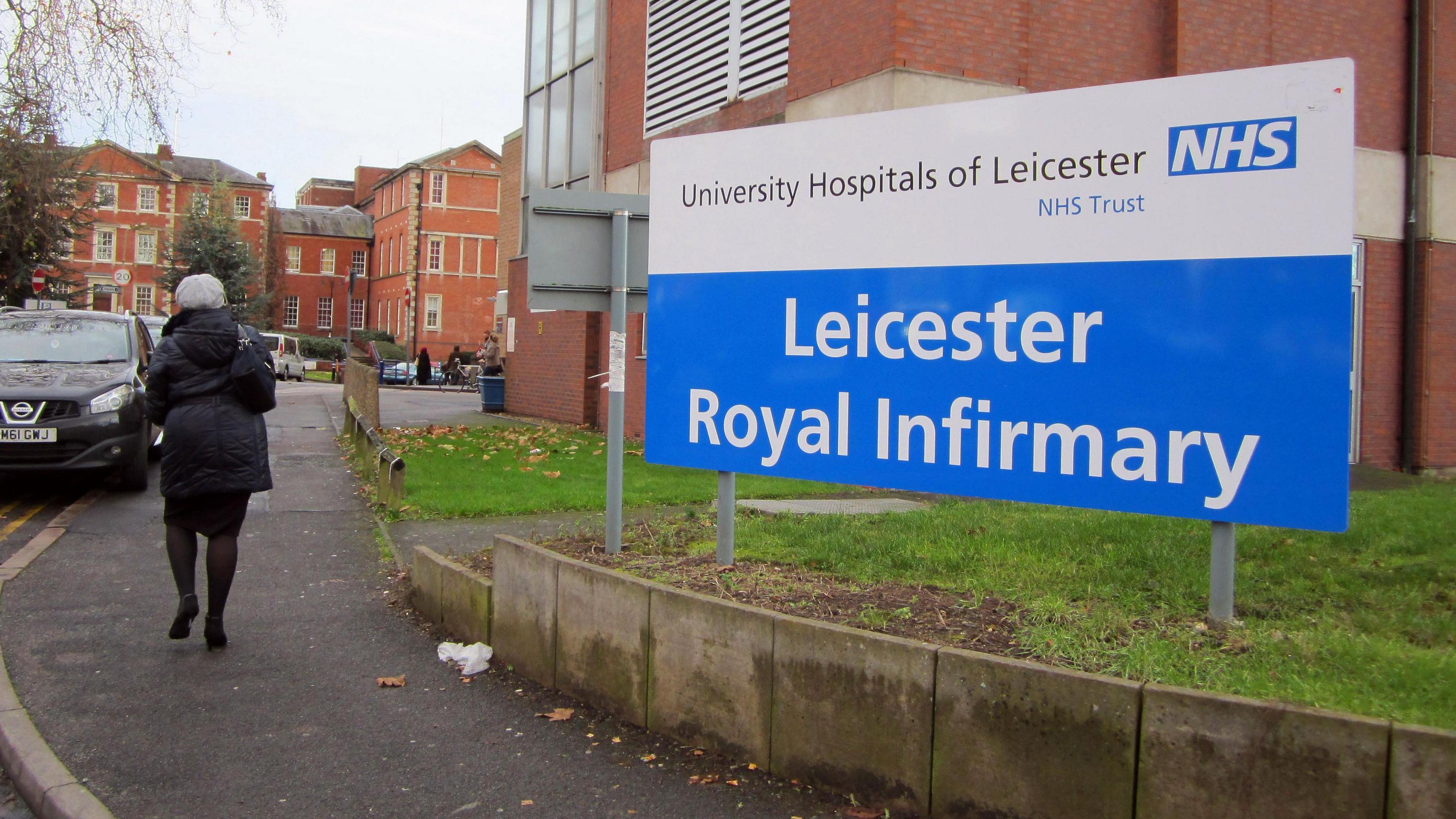 Leicester Royal Infirmary sign outside entrance with woman in hat walking past