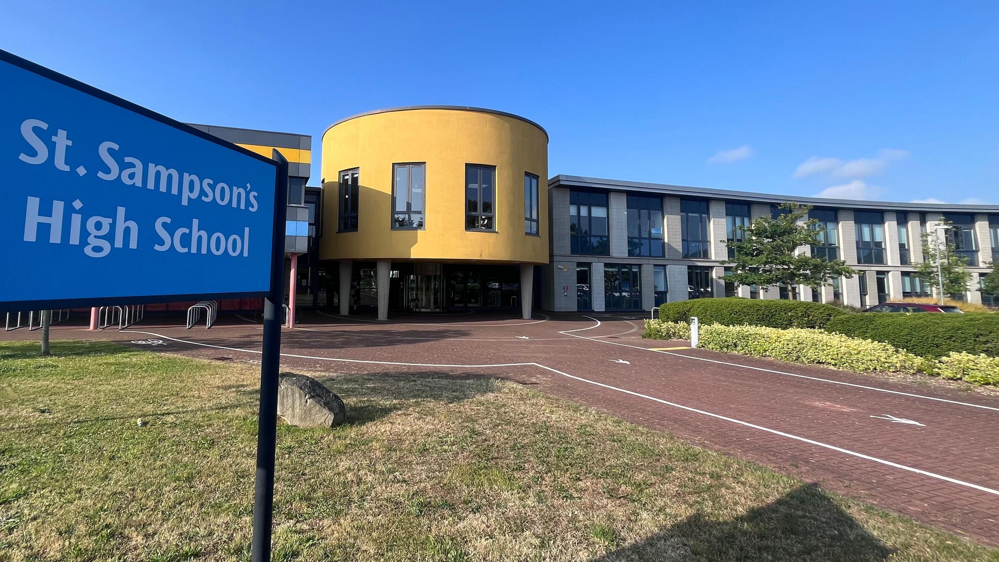 A modern-looking school with colourful, yellow walls and curves. A sign says St Sampson's School.