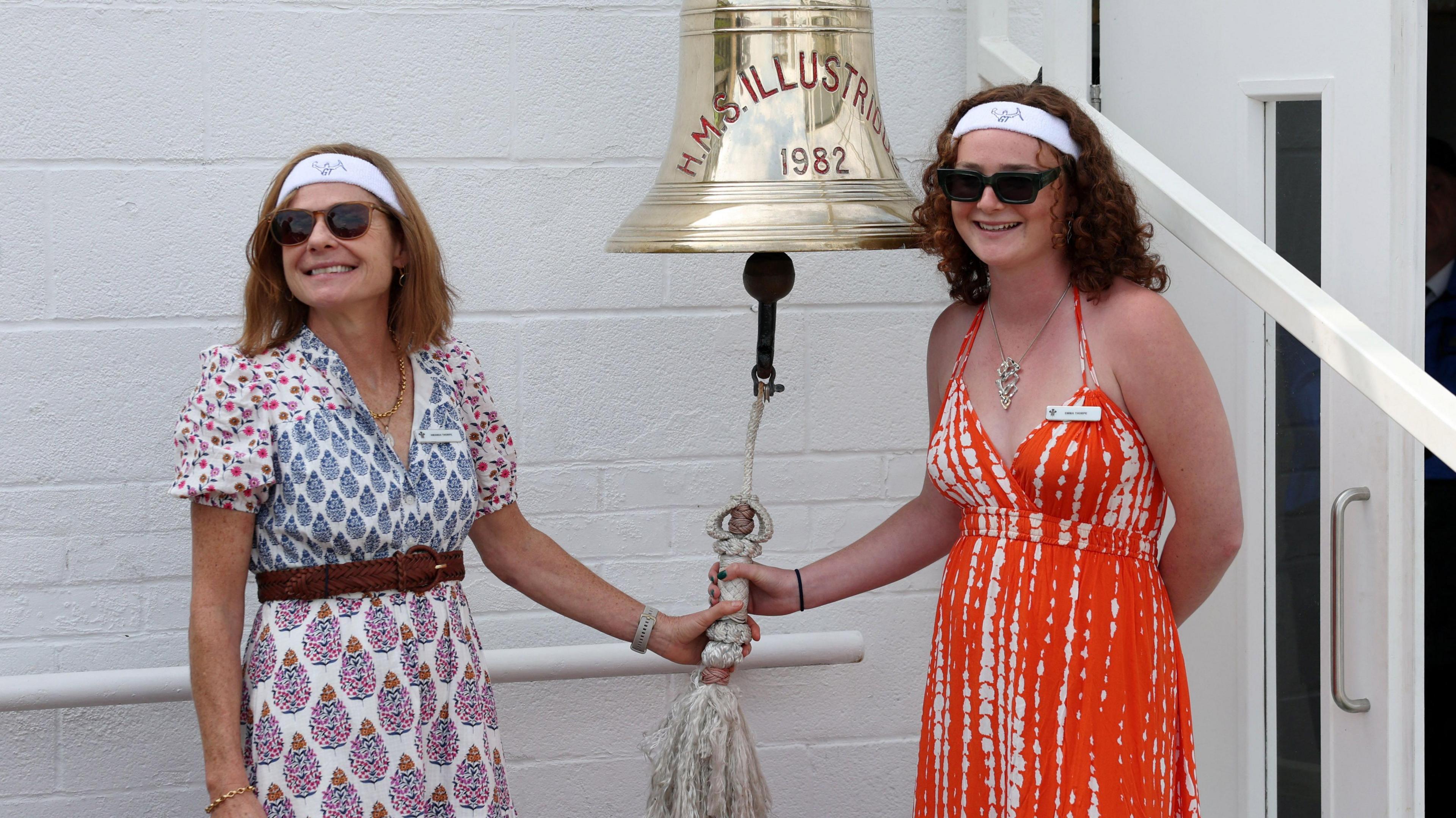 Amanda Thorpe, wife of former England cricketer Graham Thorpe and their daughter Emma Thorpe ring the bell ahead of the day's play on 'A Day for Thorpey' in support of Mind charity Action. Amanda wears a blue, red and white paisley pattern dress, and Emma wears an orange and white sundress. Both are wearing white headbands and both are holding the clapper of a bell from the ship HMS Illustrious.