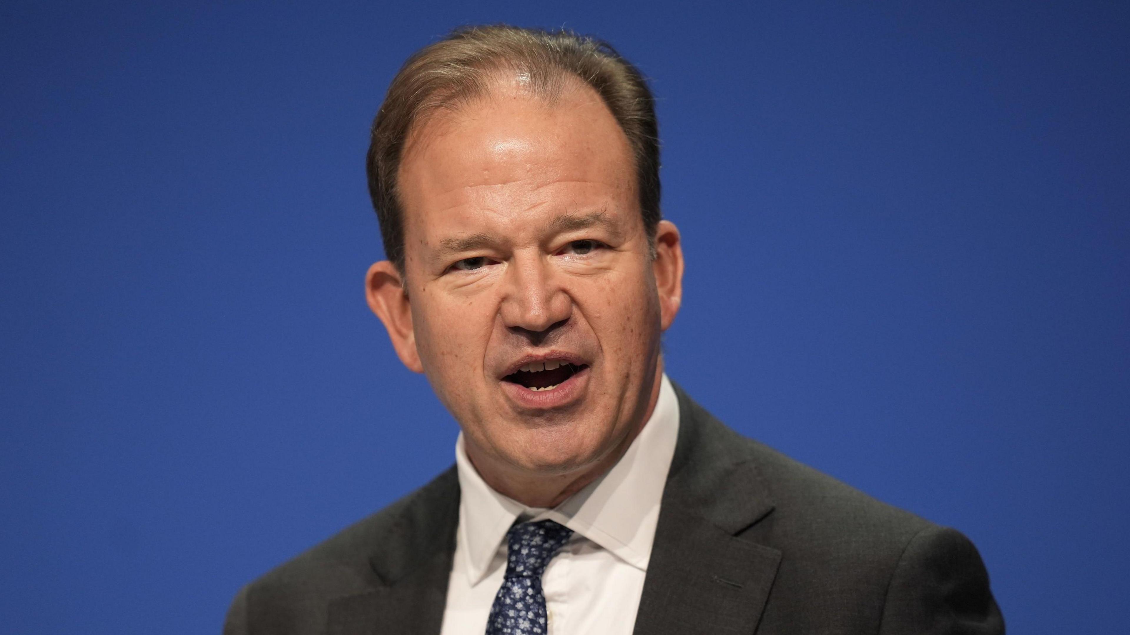 A man wearing a black suit, with a white suit and a blue dotted tie.