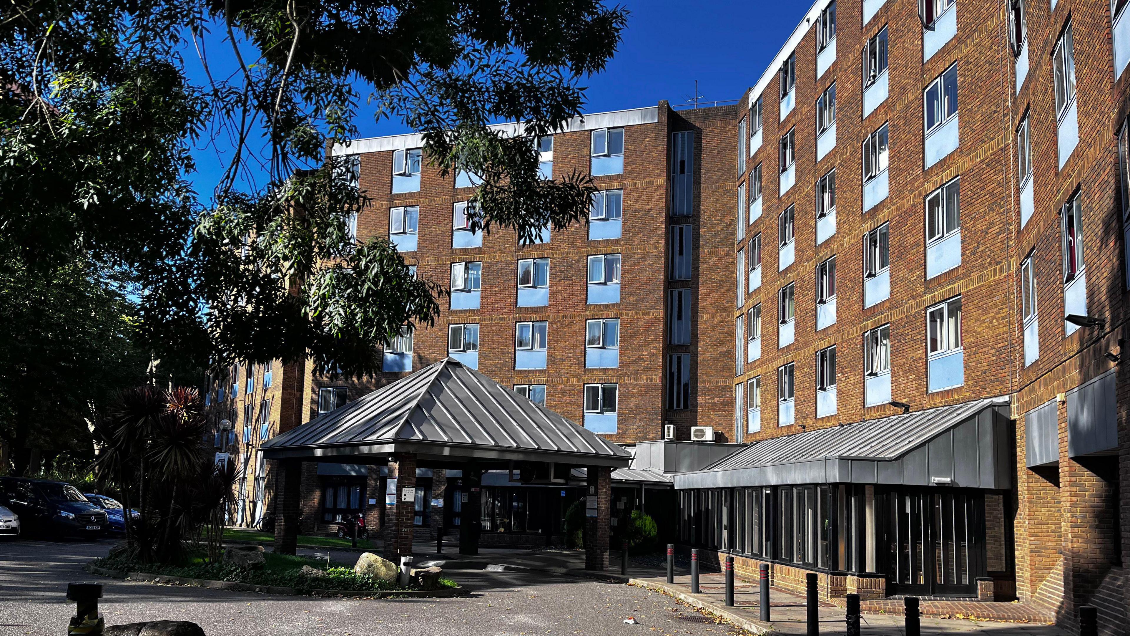 Exterior of hotel shows five storey buildings with light yellow brickwork with blue windows