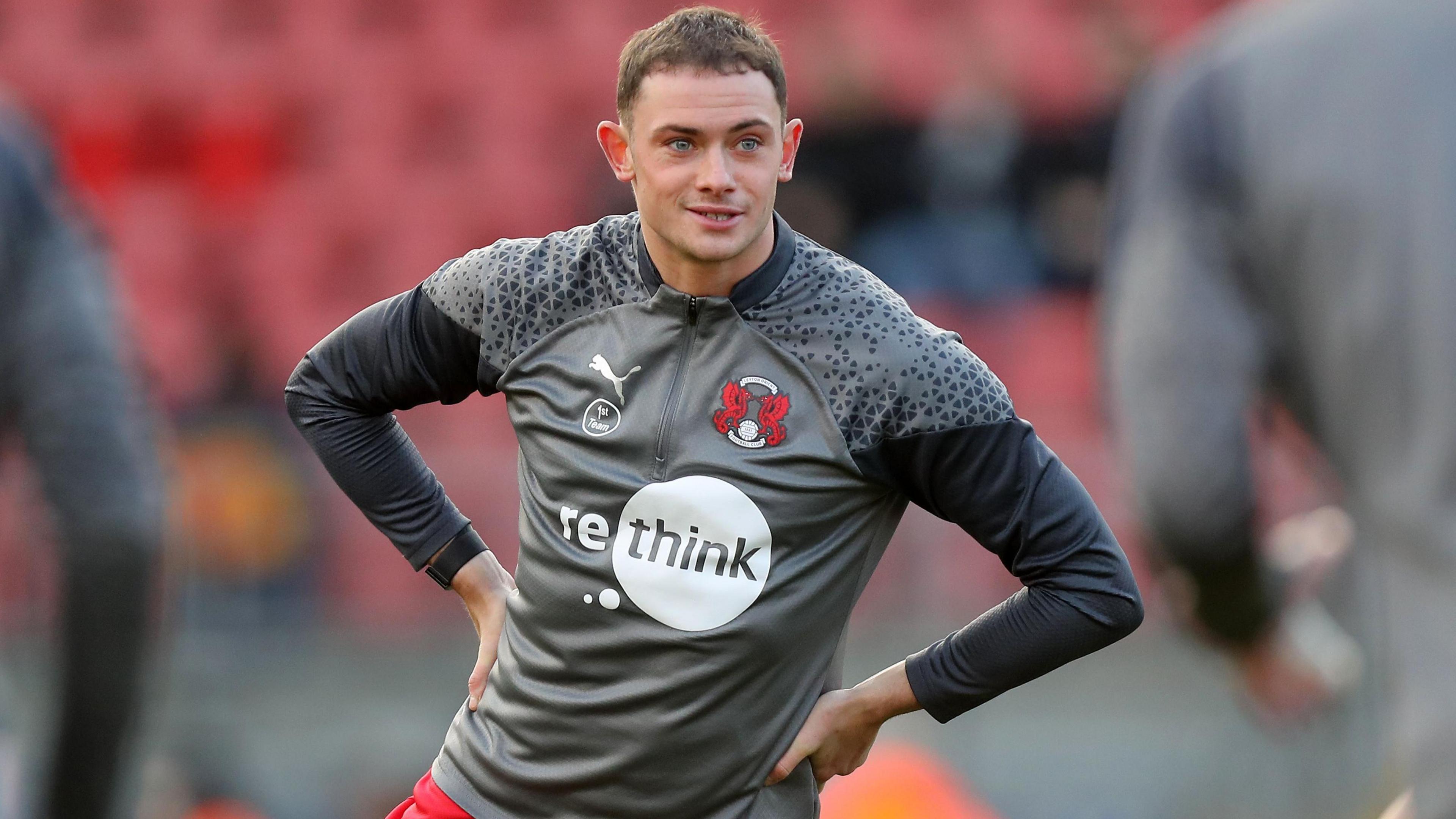 Theo Archibald, wearing a grey Leyton Orient training top and red shorts, with his hands on his hips