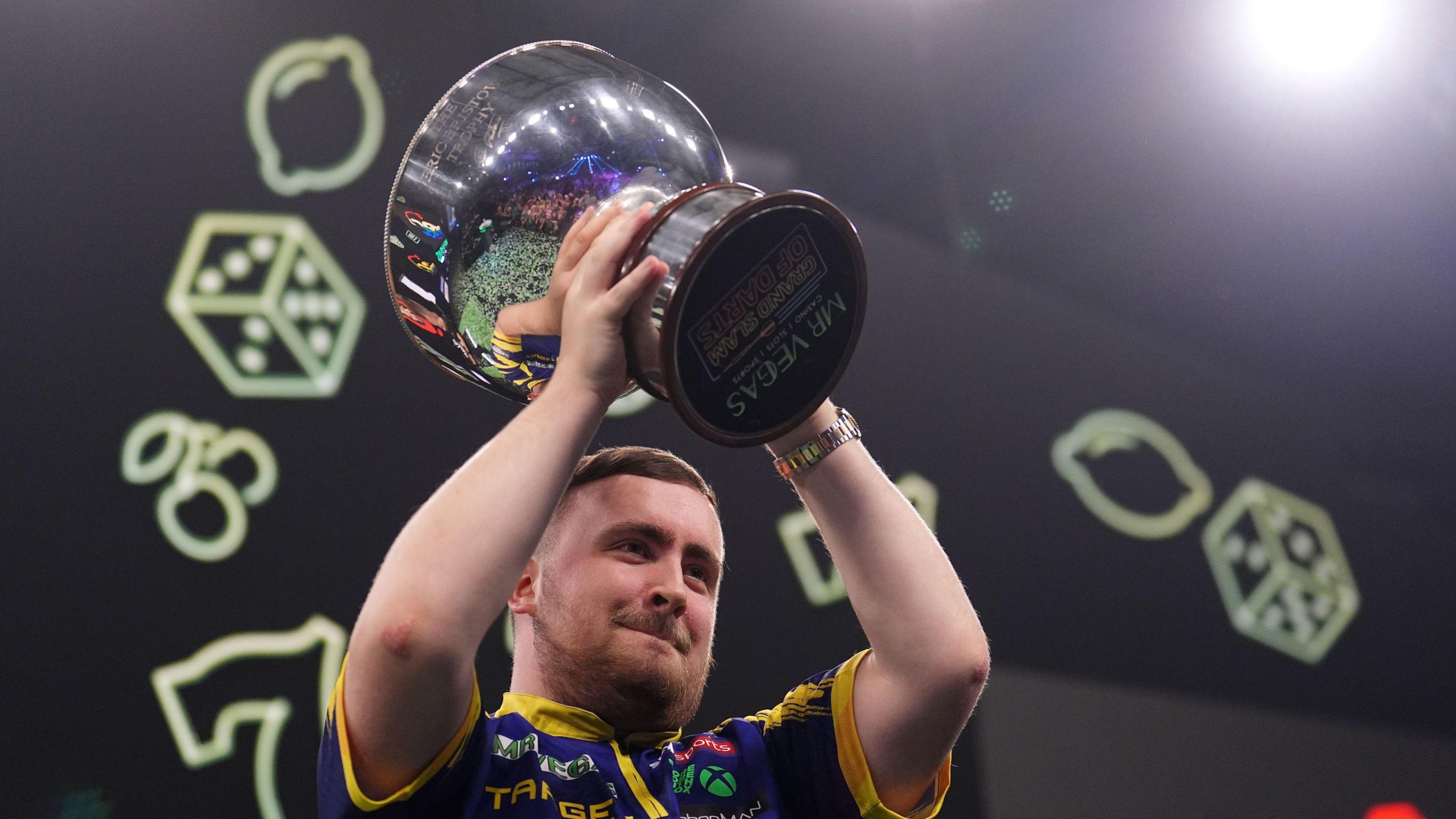 Luke Littler lifts the trophy after winning the Grand Slam of Darts final.