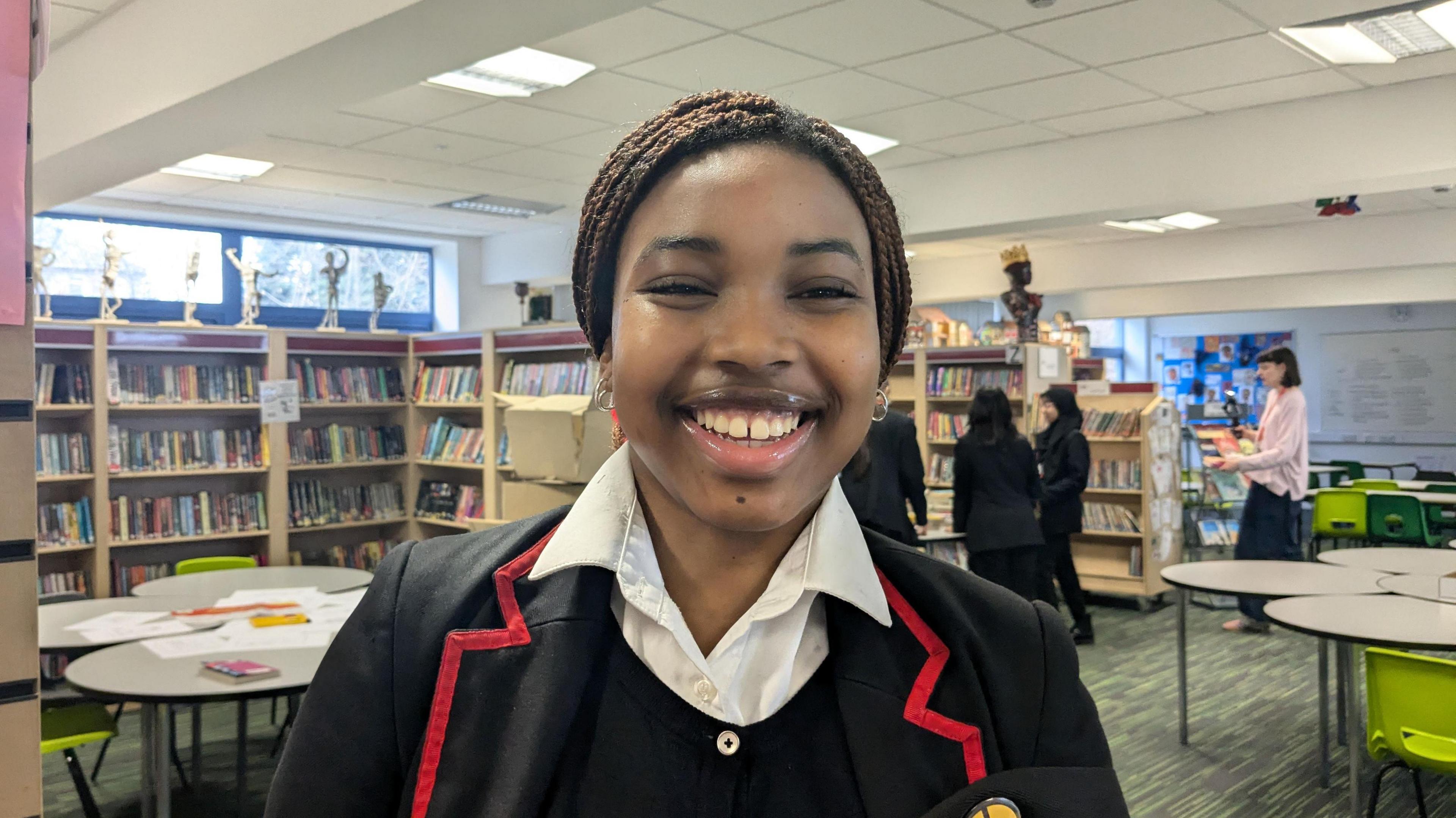 A Nigerian teenage girl with brown braided hair and school uniform. She is smiling. 