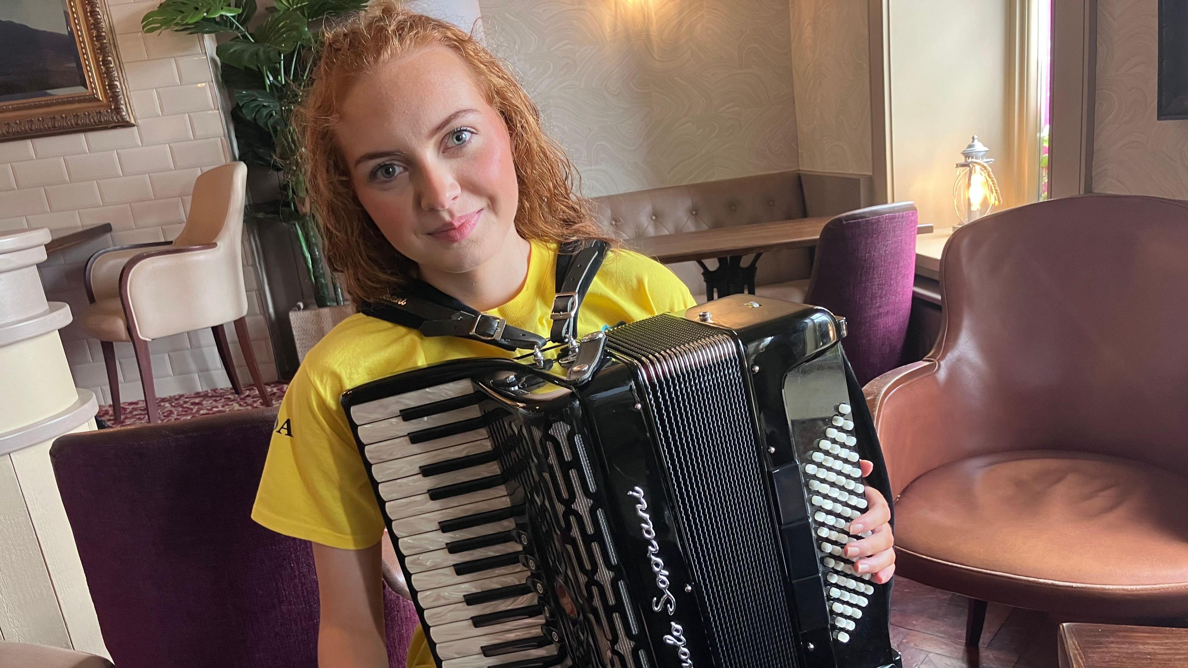 A young woman is holding an accordion. She's sitting in an empty restaurant.