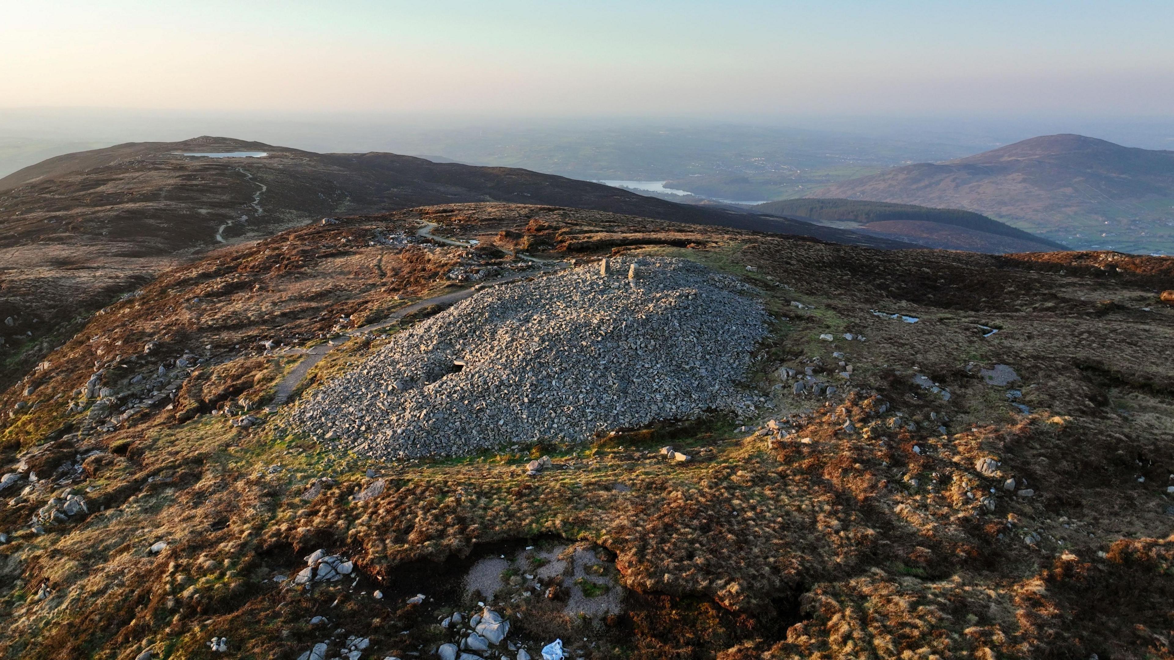 An aerial shot of the Slieve Gullion passage tomb in Armagh. A birds-eye view showing a very large pile of grey rocks on top of a mountain.