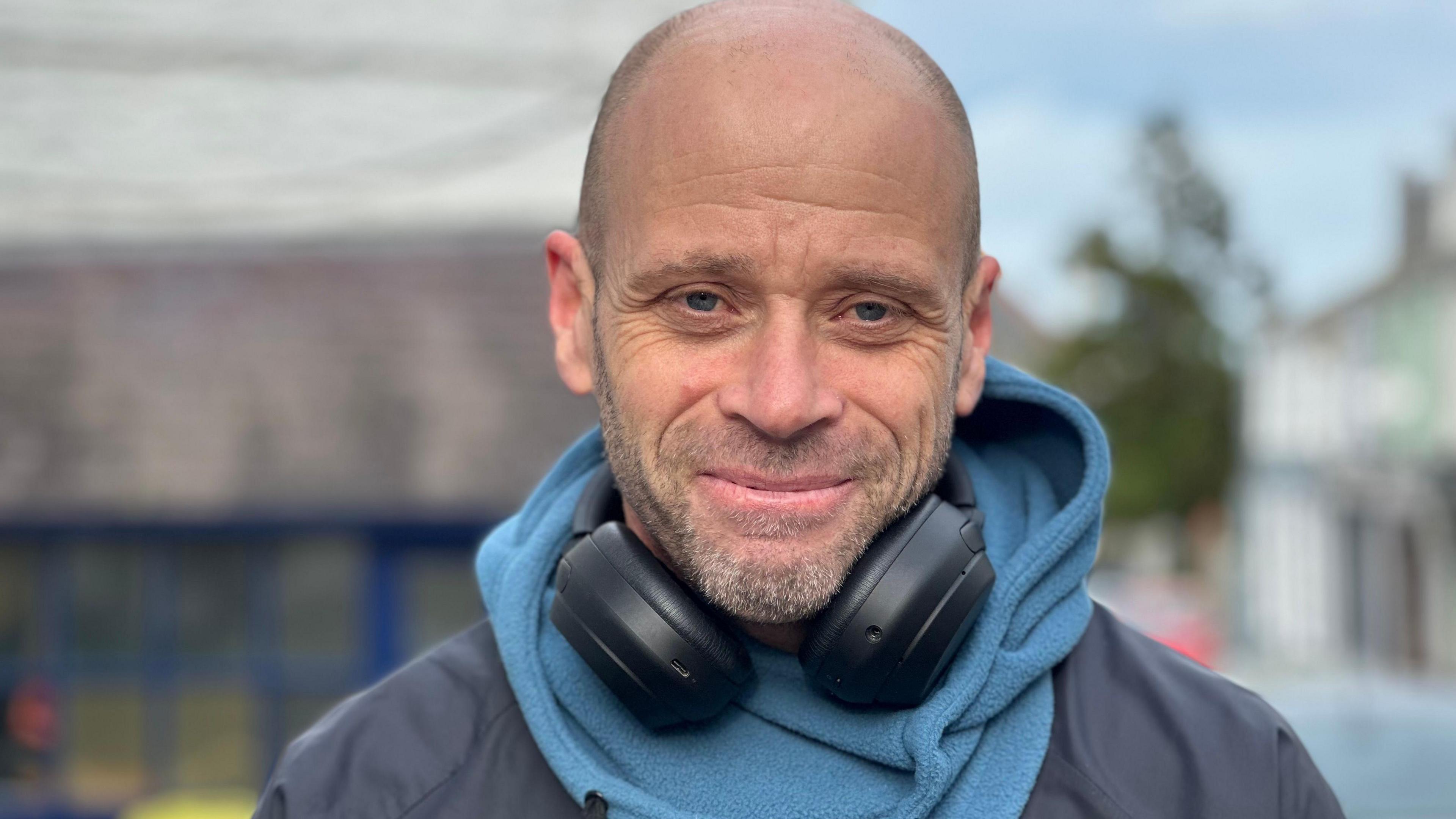 Picture of bald man in a coat wearing headphones around his neck 