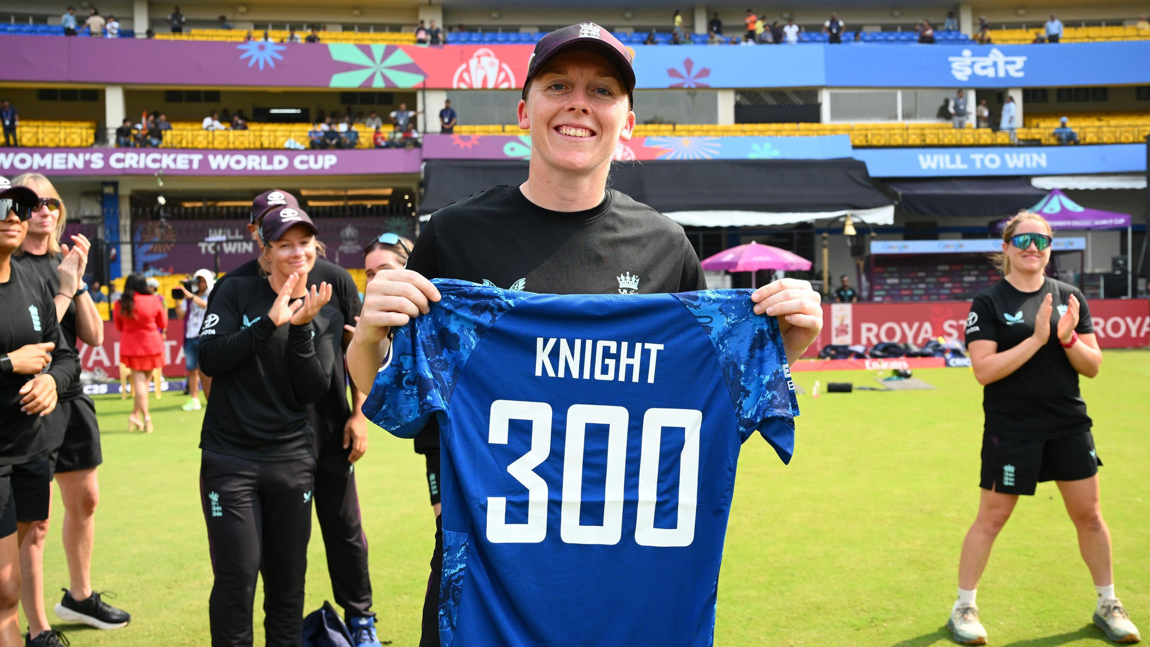 Heather Knight holding an England shirt with Knight 300 on the back