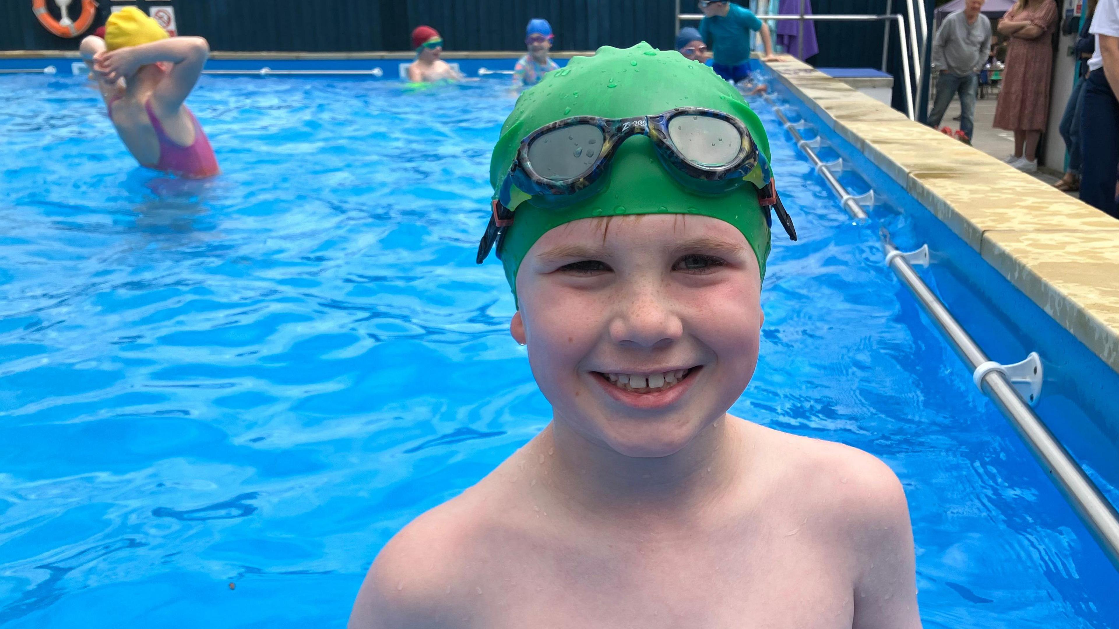 Nevin smiles. He is wearing a green swimming hat and dark goggles over his head.