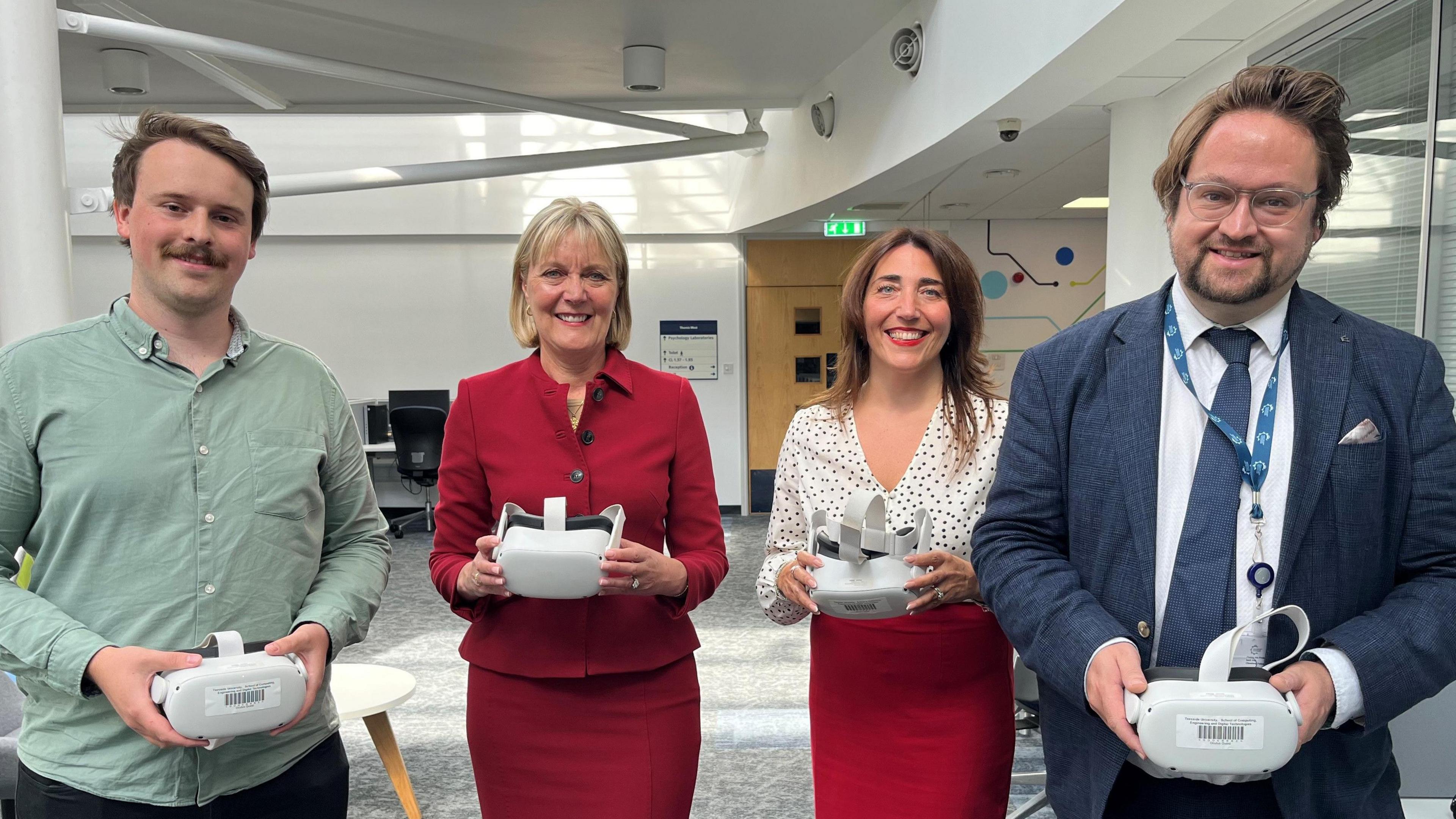 Four smiling people, two men and two women, holding VR headsets.