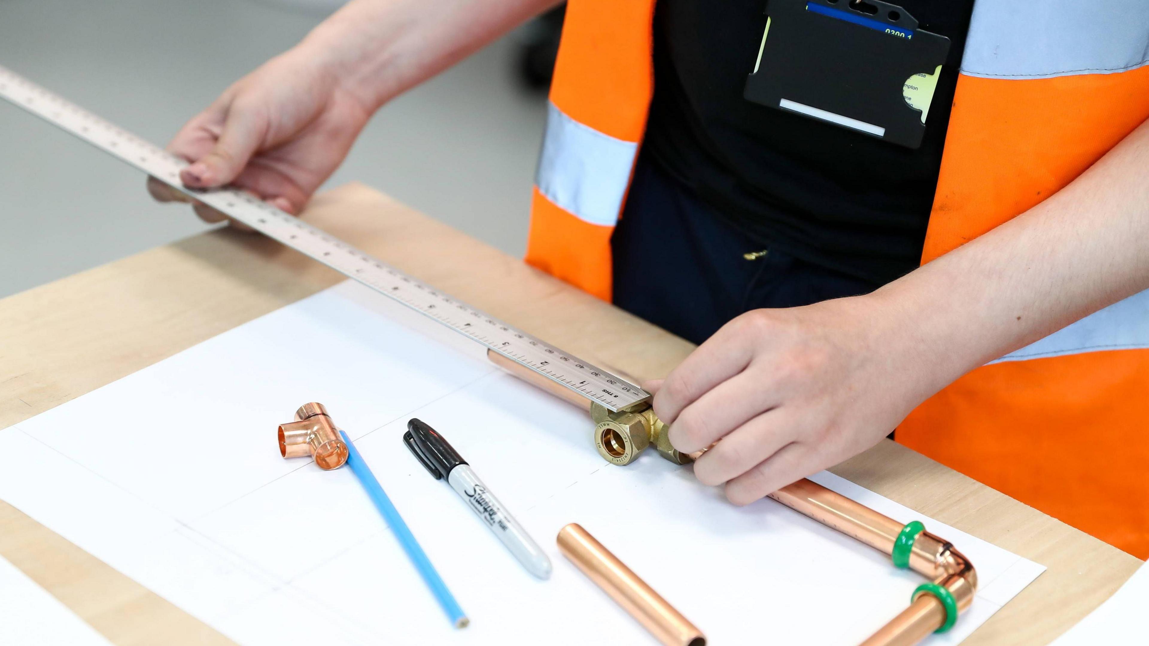 Person using a ruler to measure some metal piping on a wooden desk