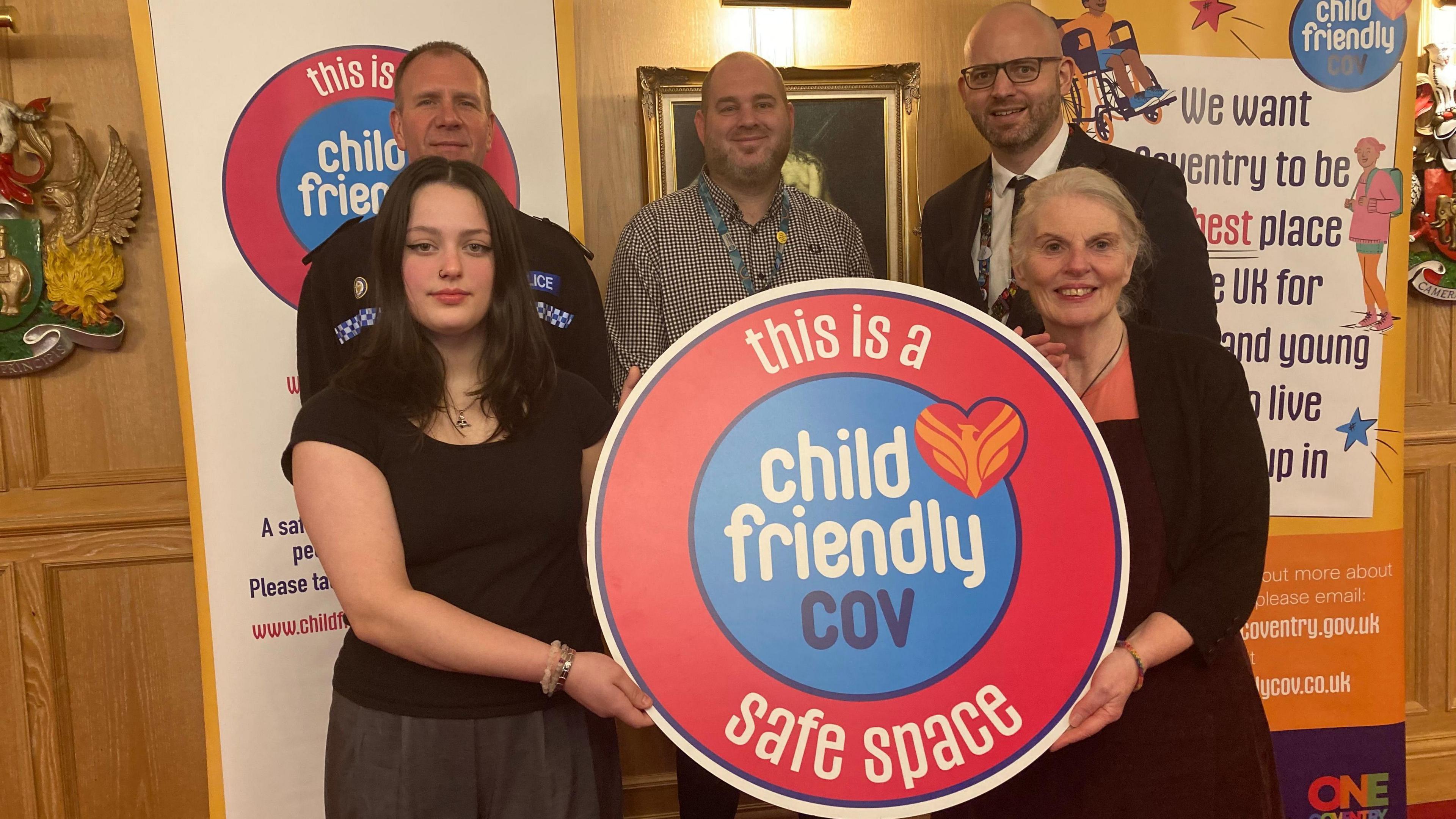 Men and women at the council house hold up the "Child Friendly Cov" sign.