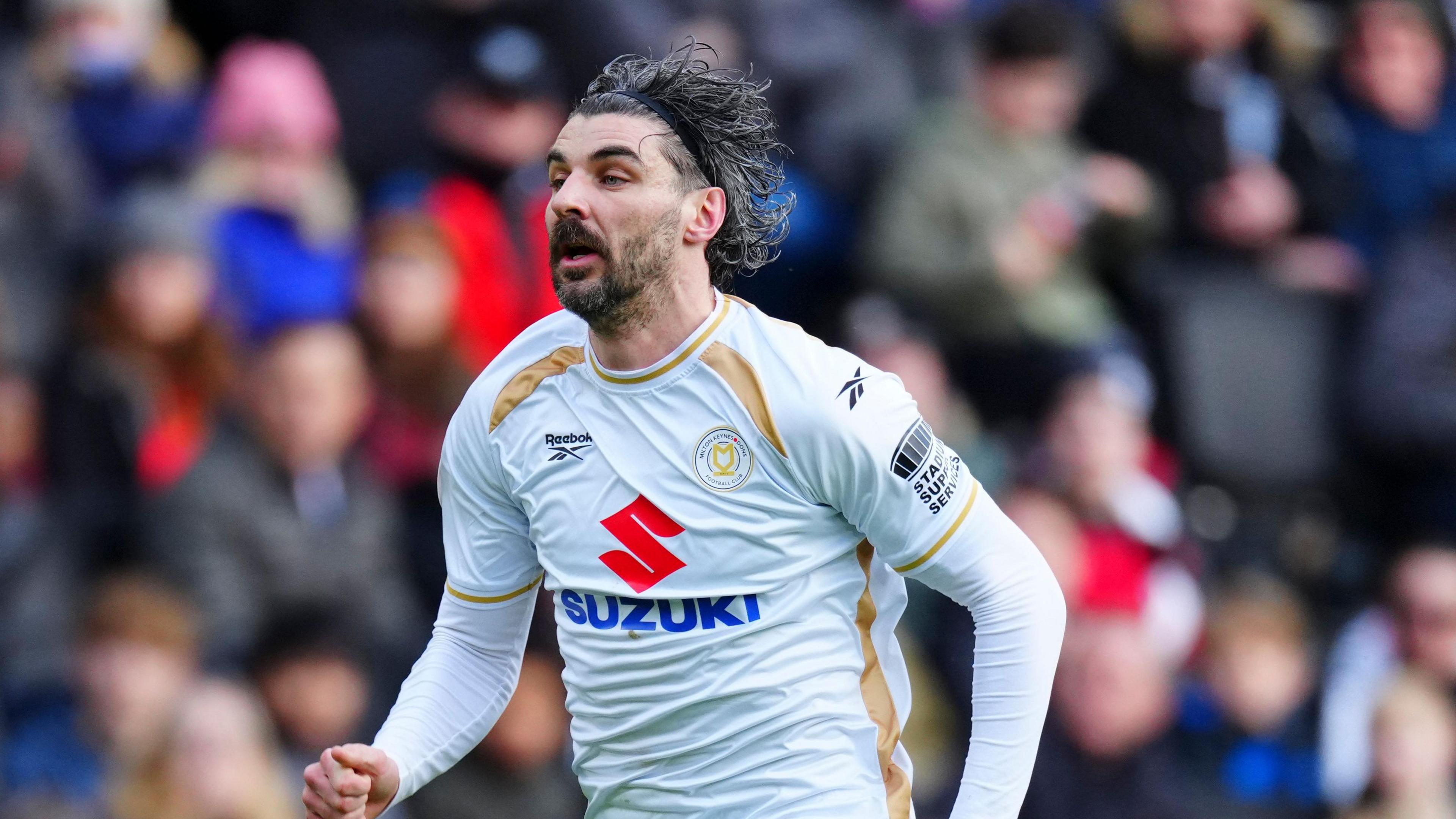 A photo of Callum Paterson running during a match while wearing a white and gold MK Dons kit