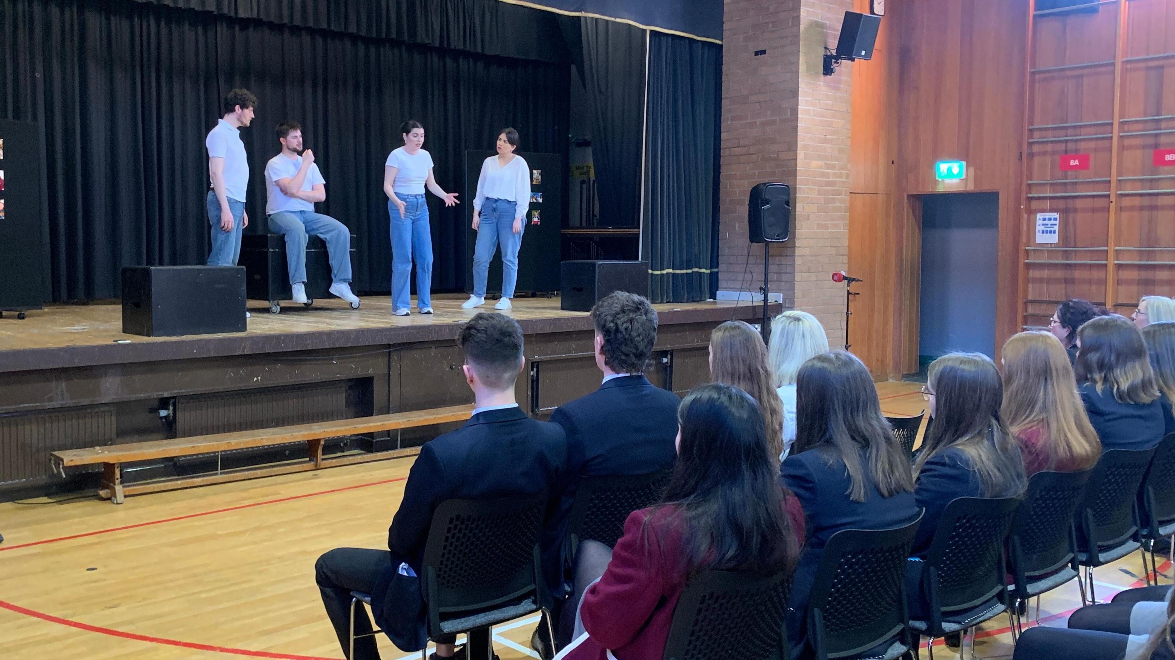 Actors on a stage with an audience of students looking on