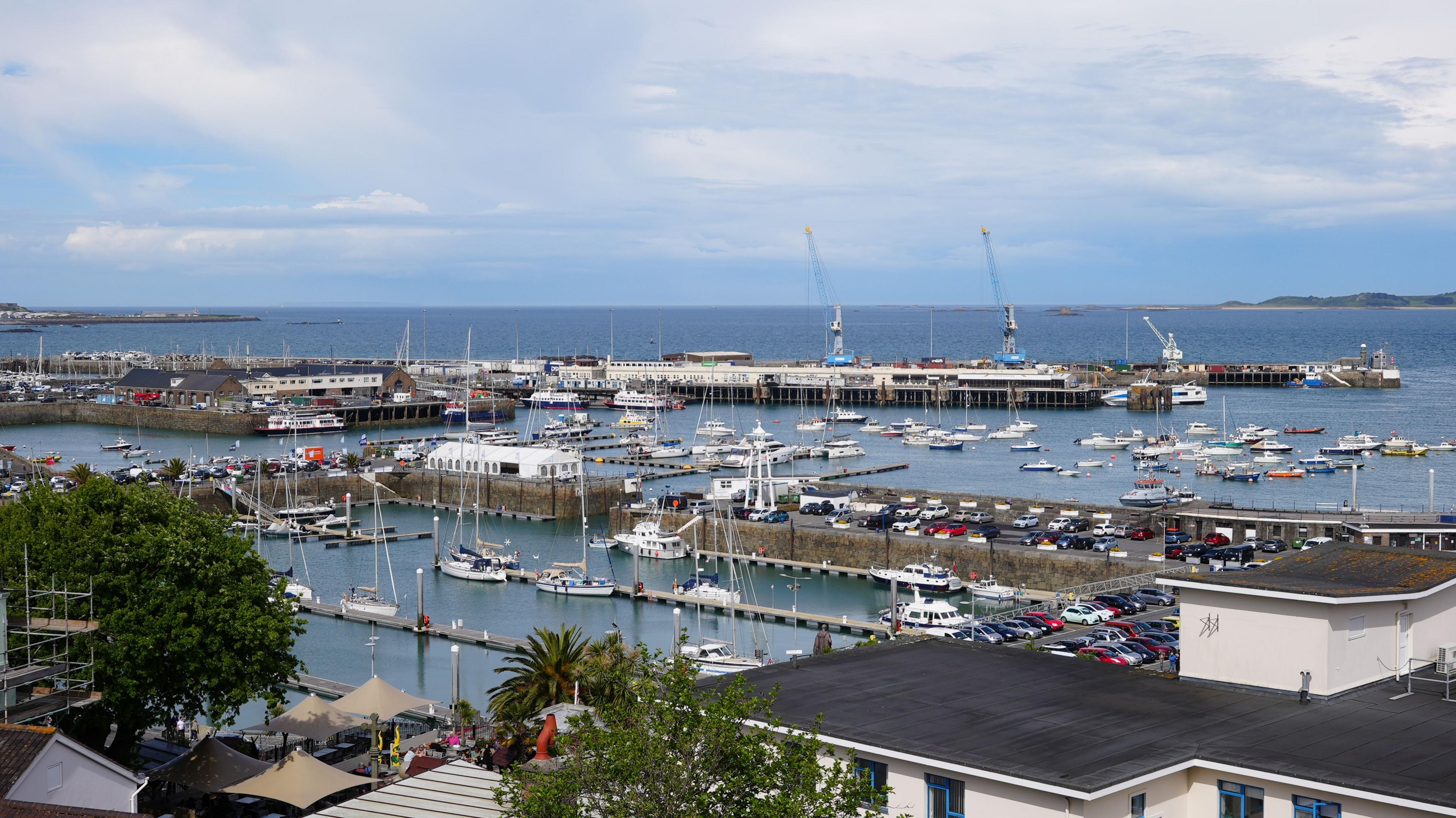 Guernsey's St Peter Port harbour. It shows boats on the water, cranes and car parking facilities. 
