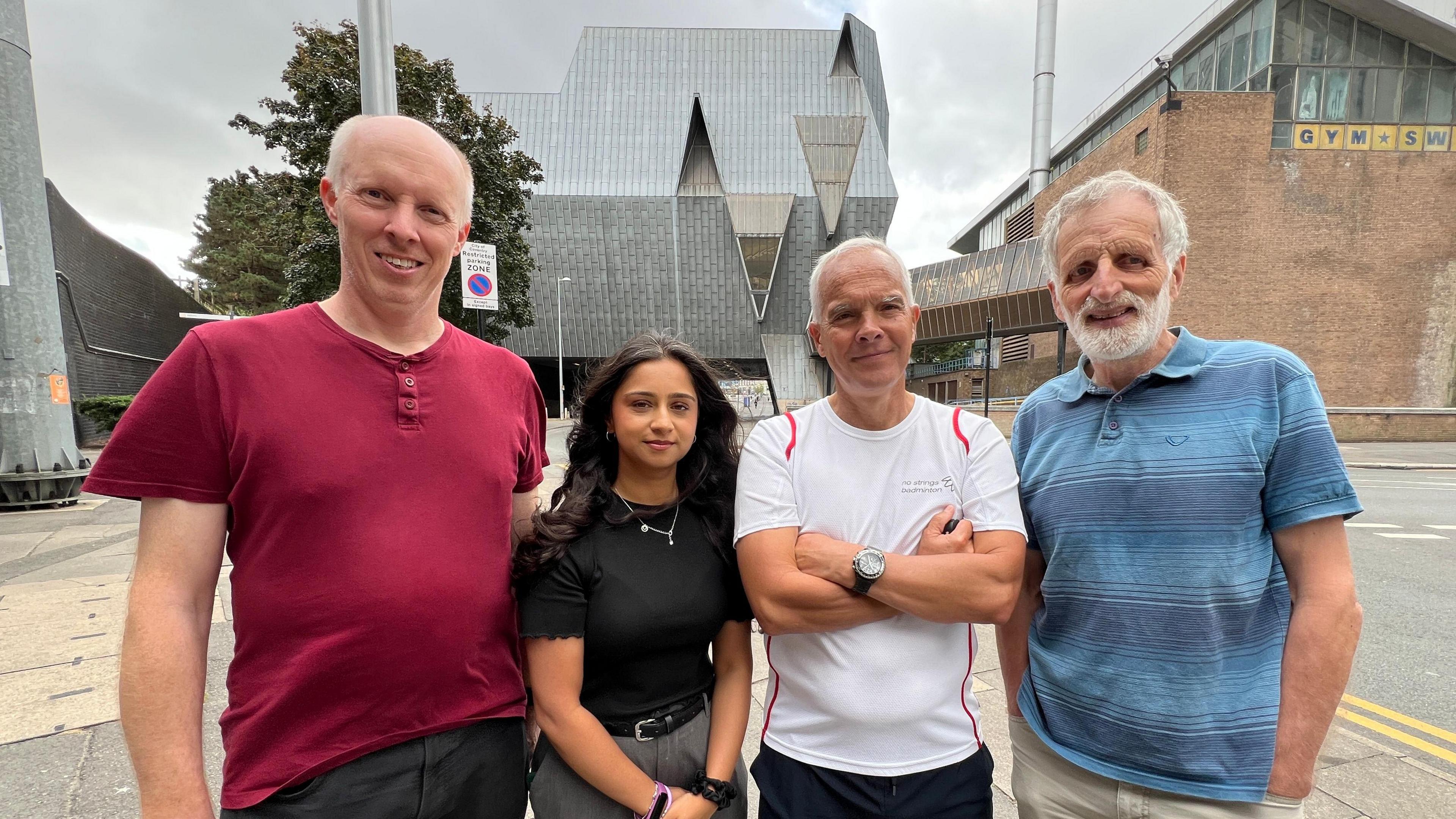Campaigners are calling for the reopening of Coventry Leisure Centre, known locally as The Elephant. From left to right, Justin Bissell has white hair and is wearing a red T-shirt and grey trousers; Kauser Husain has long dark hair and is wearing a black T-shirt, silver chain and grey trousers; Richard Jardim has white hair and is wearing a white T-shirt and black trousers; and Rick Watson has grey hair and is wearing a blue polo shirt and cream trousers. They are standing in front of the large grey elephant-shaped leisure centre building and are looking at the camera.
