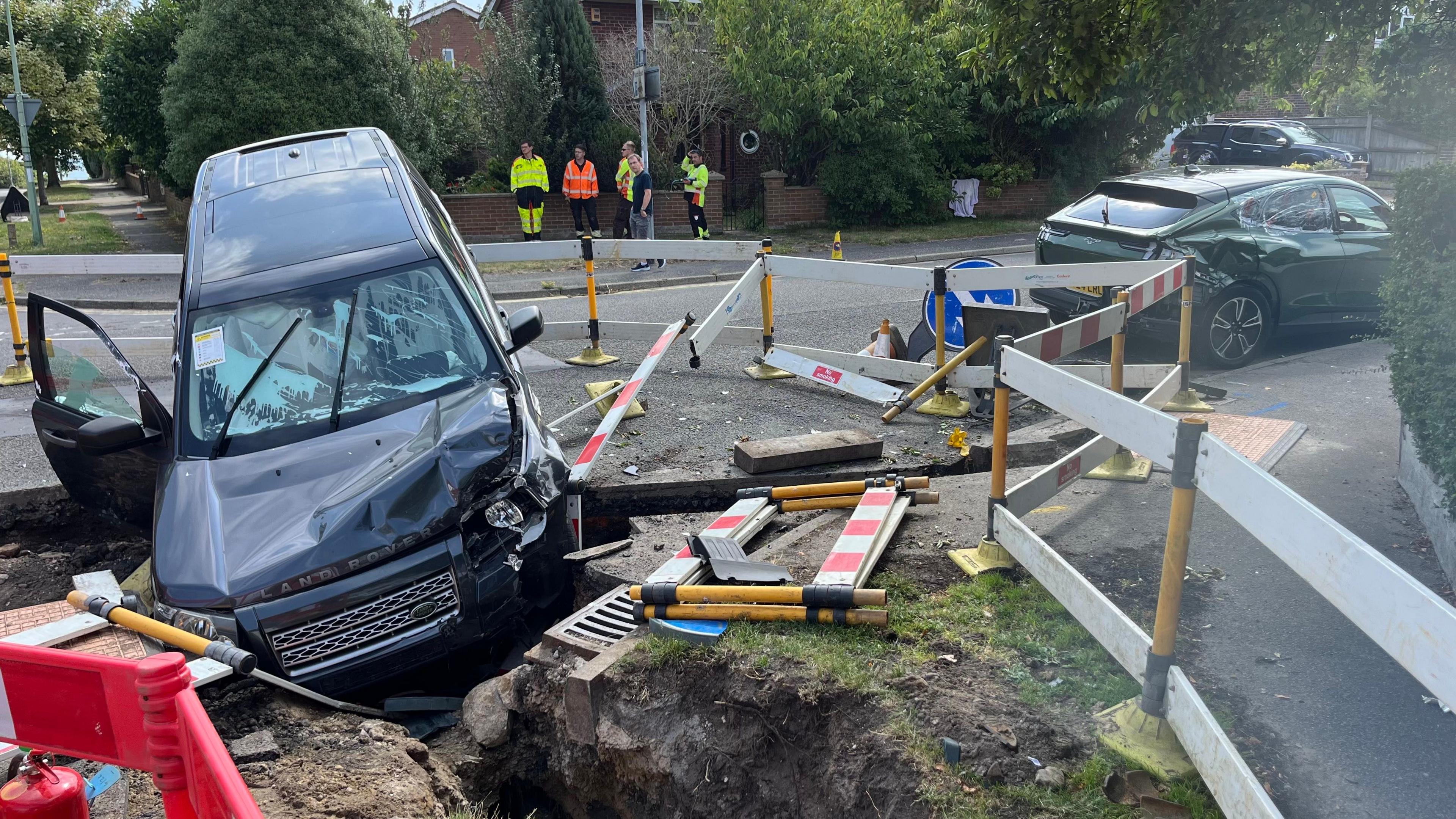 A wider view of the collision. White paint can be seen covered all over the Land Rover windshield. Another damaged car can be seen nearby.