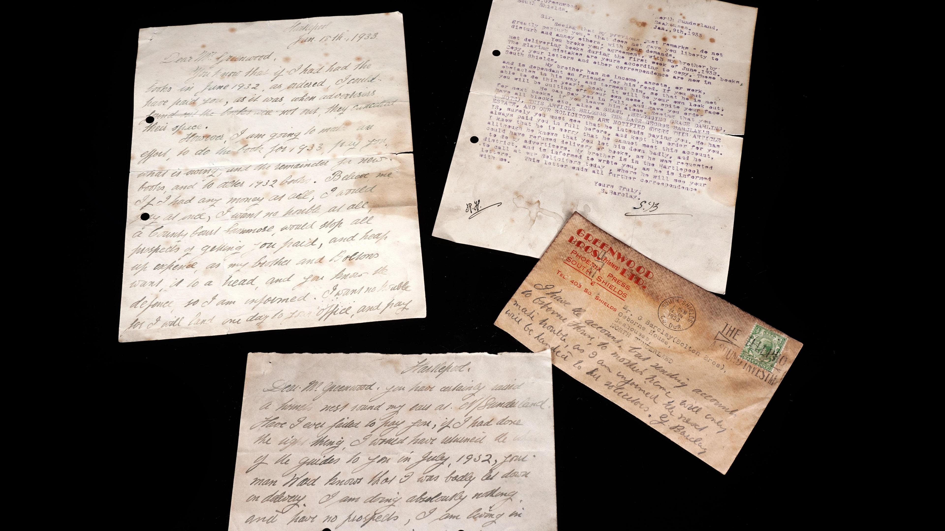 Four pieces of paper sit on a black table. The papers are tired and stained brown, showing their age and having handwriting on.