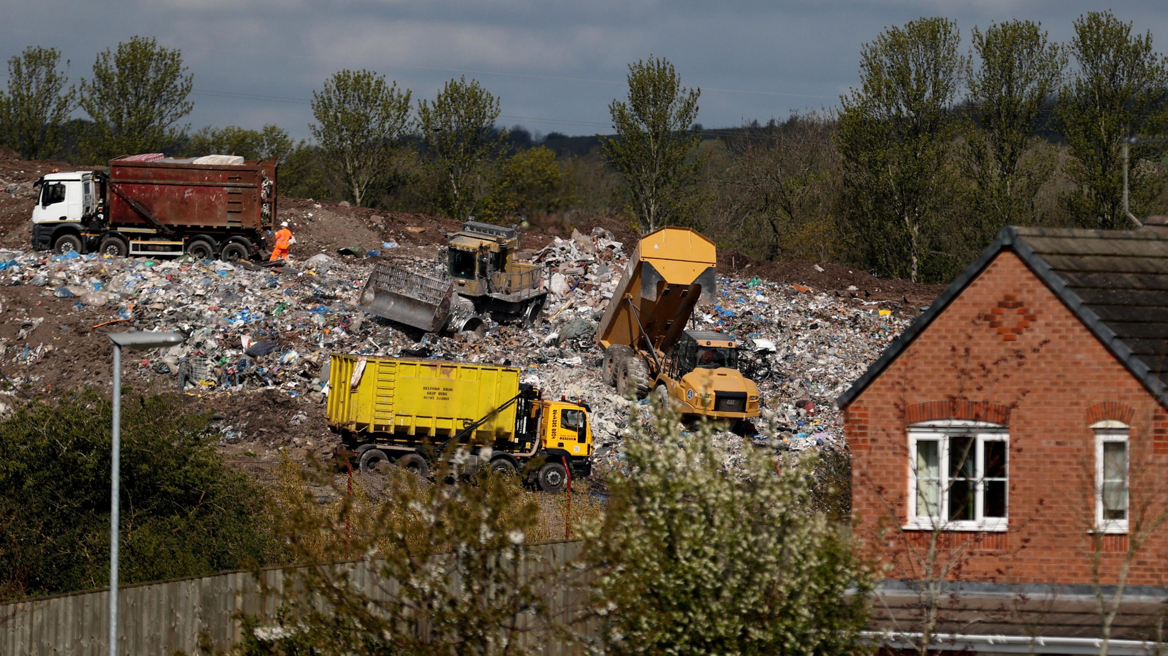 A house on the right hand side with a waste management site in the background. there are four lorry vehicles on the waste.