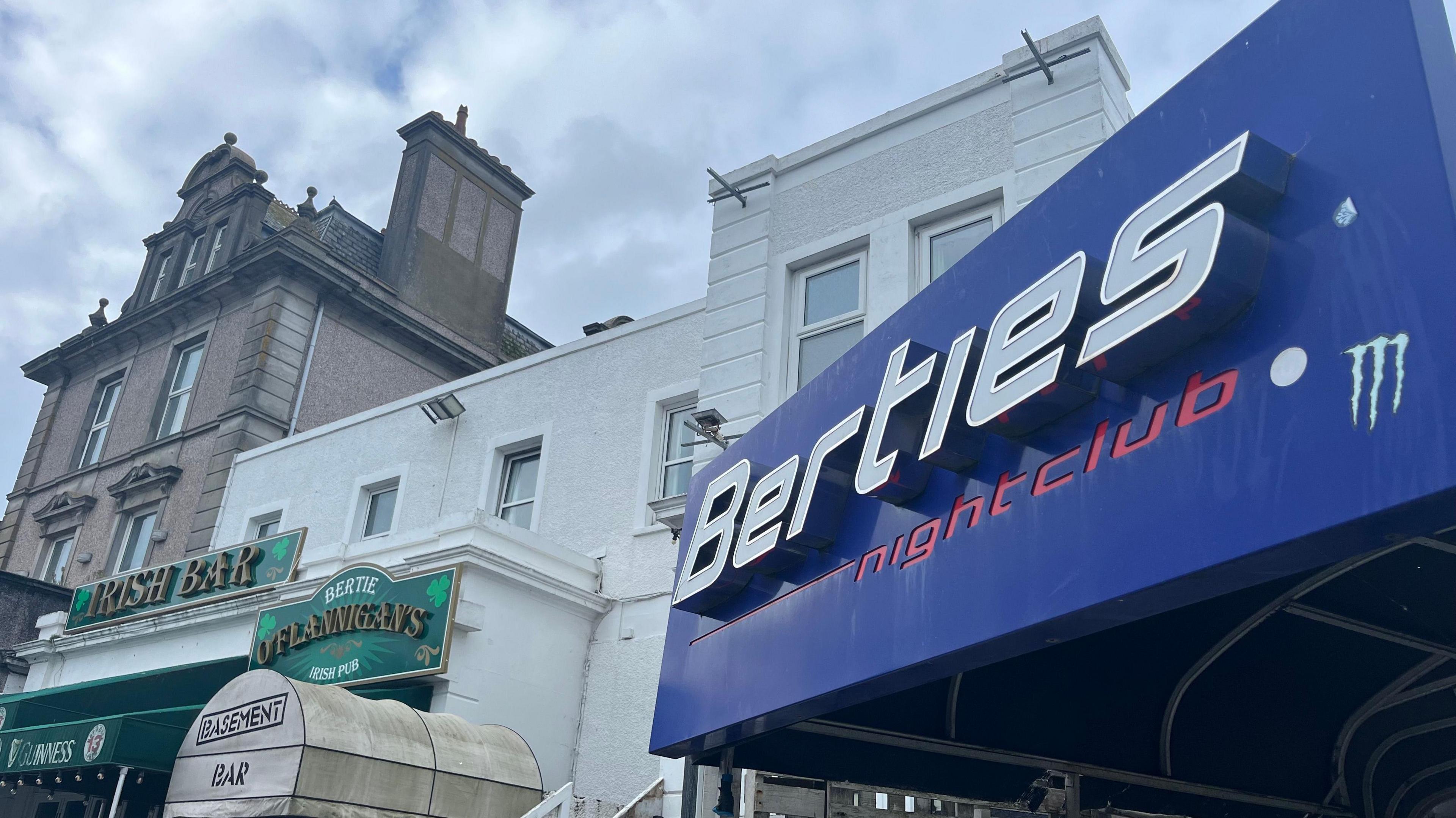 A nightclub sign saying "Berties" is see on the right in blue and silver, while, on the left, a pub called O'Flannigan's Irish Bar can be seen with a green banner above the door 