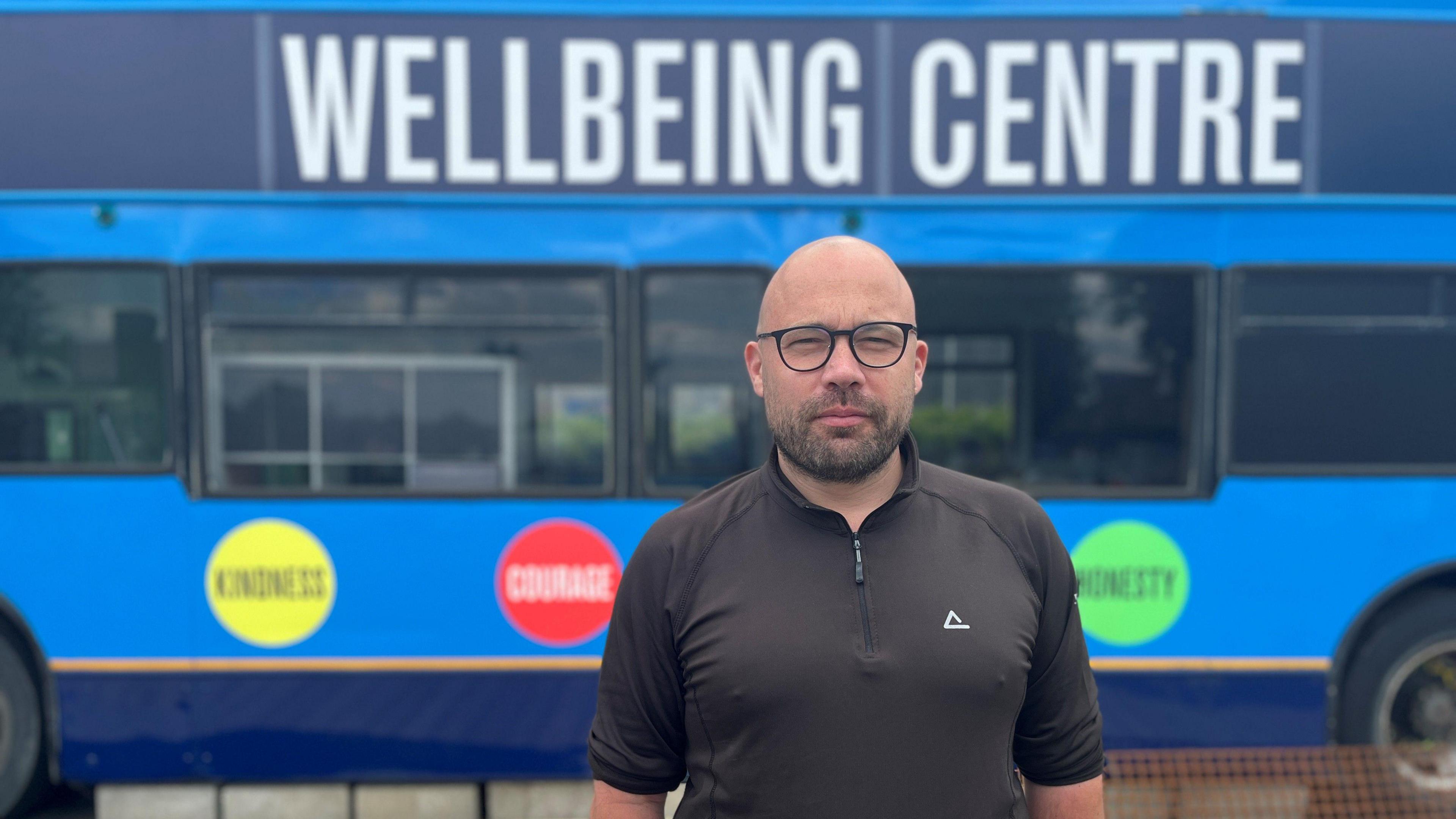 Matt Paterson standing in front of a blue bus with Welfare Centre in large white text