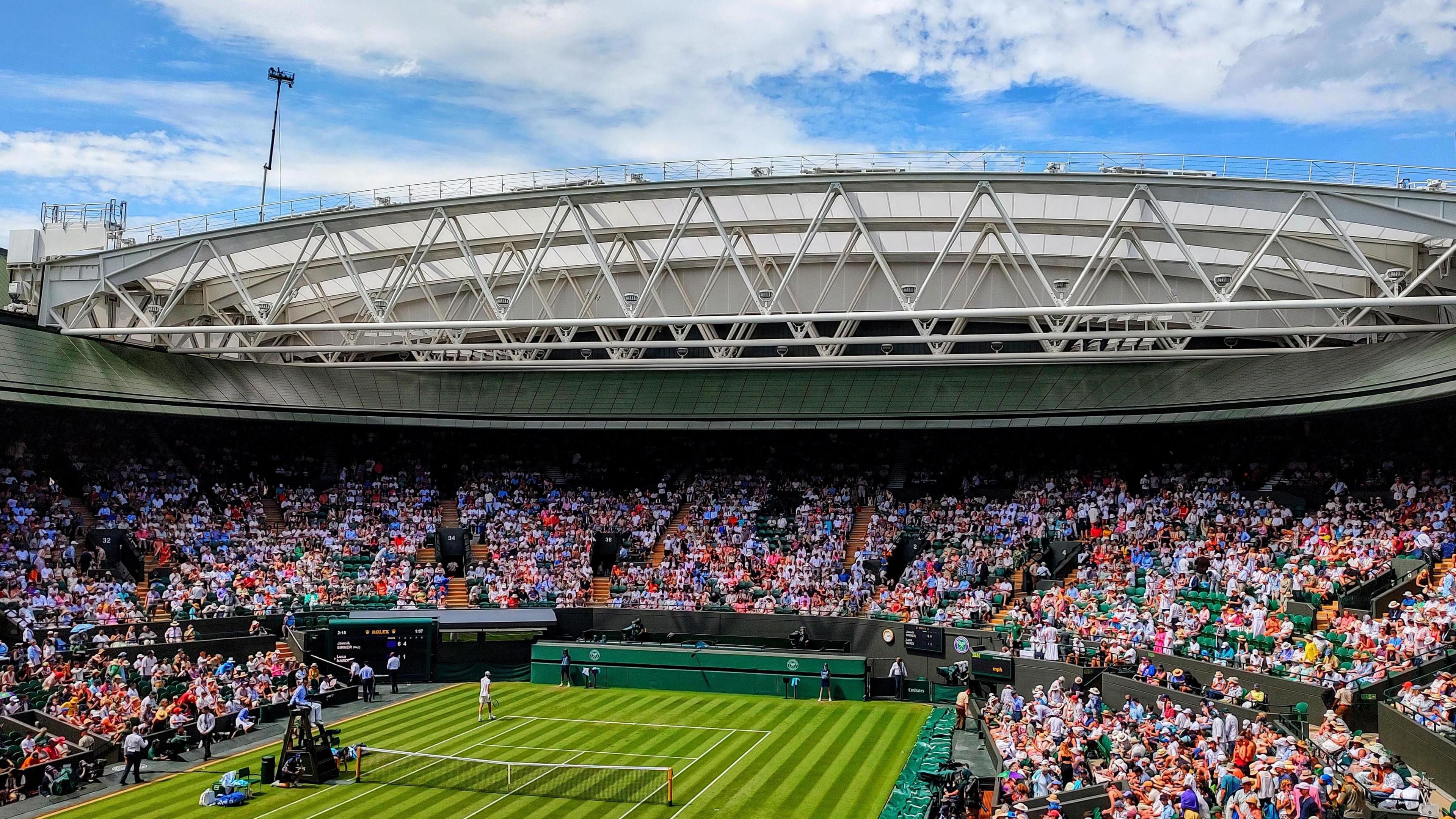 Spectators in the sunshine watching tennis at Wimbledon's Court One