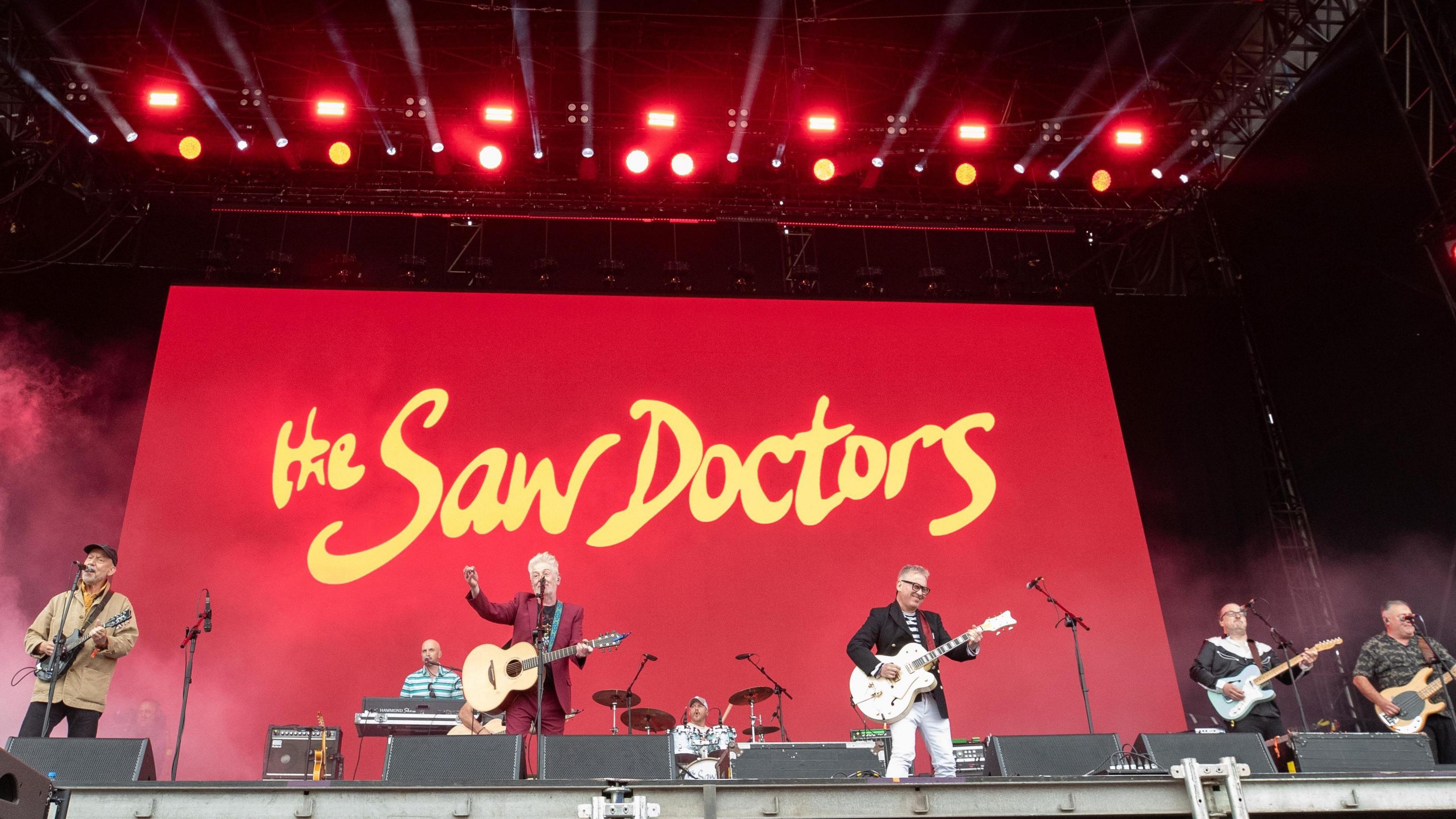 Band on stage in front of a large display that says "The Saw Doctors"